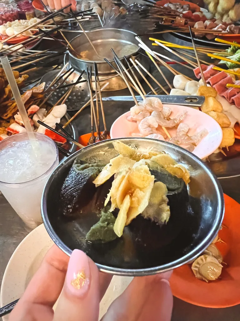 Stuletnie jajko podane z imbirem i warzywami w malezyjskim stylu Lok Lok, na tle stołu pełnego szaszłyków do gotowania w bulionie