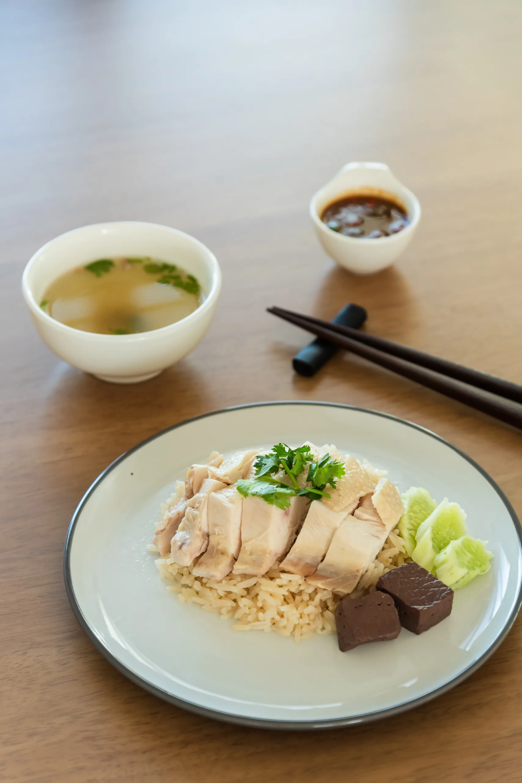 Hainanese chicken rice – gotowany kurczak podany na aromatycznym ryżu z plasterkami ogórka, kostkami krwi, sosem z fermentowanej soi i bulionem