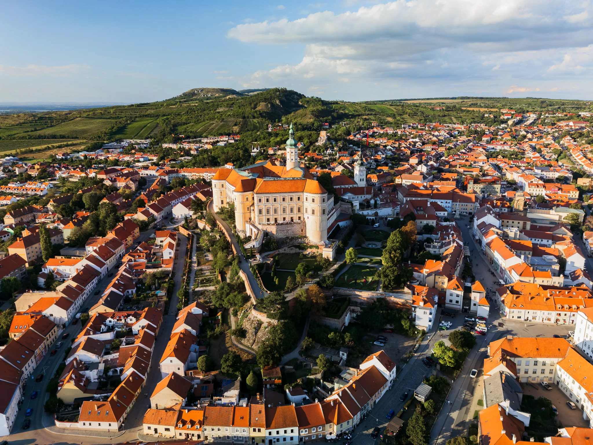 Panorama Mikulova w Czechach – zamek na wzgórzu otoczony czerwonymi dachami starego miasta i zielonymi wzgórzami w tle.
