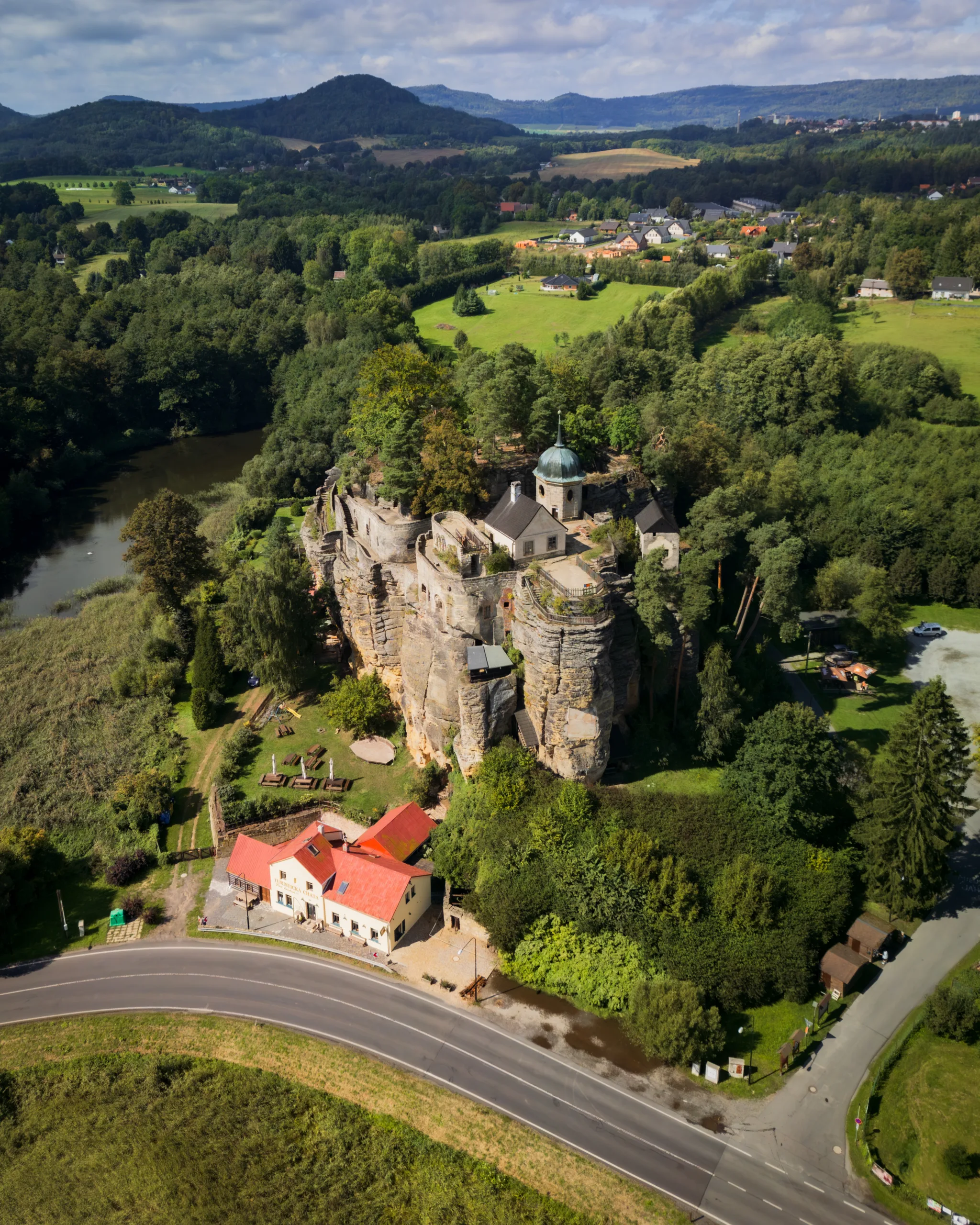 Zamek Sloup wzniesiony na skale piaskowcowej, widok z lotu ptaka na warownię otoczoną zielenią i okoliczne wzgórza północnych Czech.