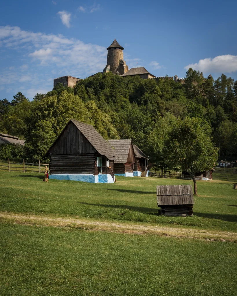 Drewniane chaty skansenowe na tle zielonego wzgórza z górującym nad nimi zamkiem - Zamek w Lublowej
