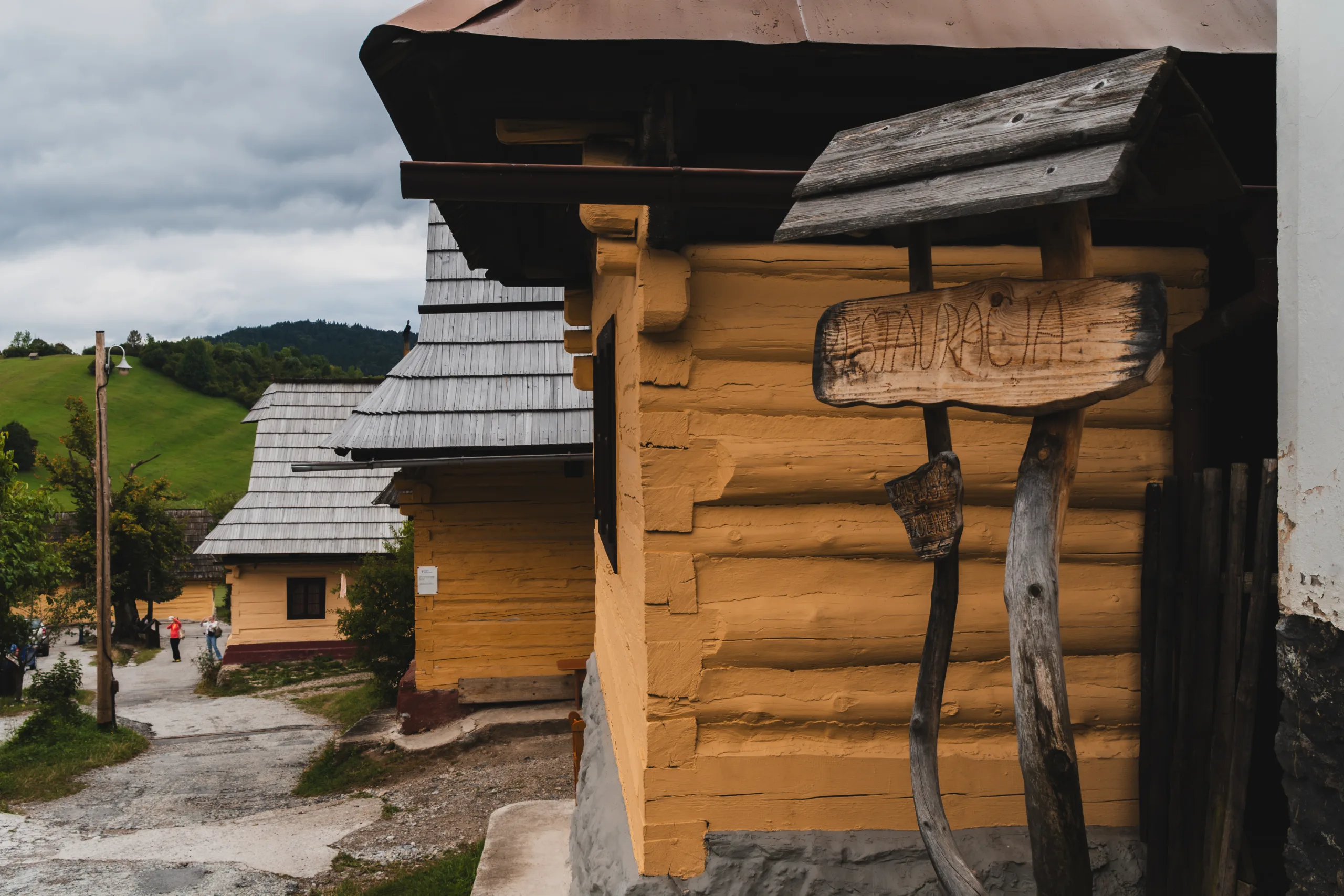 Zabytkowe drewniane chaty we wsi Vlkolínec na Słowacji, z widocznym szyldem restauracji i zielonymi wzgórzami w tle.