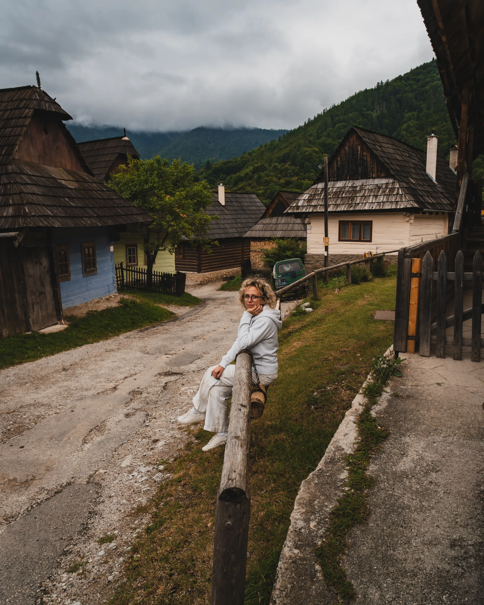 Ulica we wsi Vlkolínec na Słowacji z tradycyjnymi drewnianymi domami, wpisanej na listę UNESCO, z kobietą siedzącą na drewnianej poręczy.