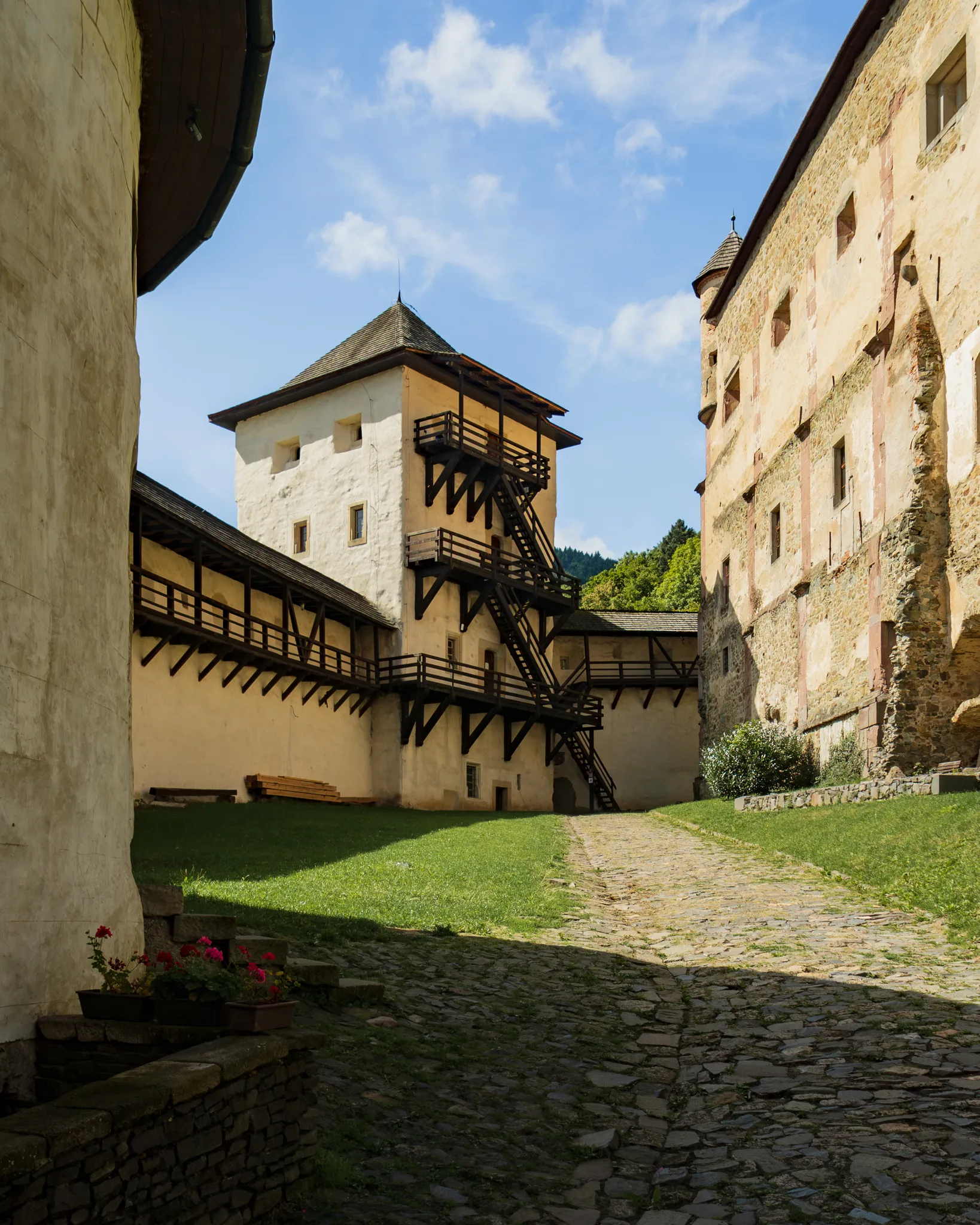 Dziedziniec Starego Zamku w Bańskiej Szczawnicy z kamienną wieżą i drewnianymi schodami prowadzącymi na mury obronne.