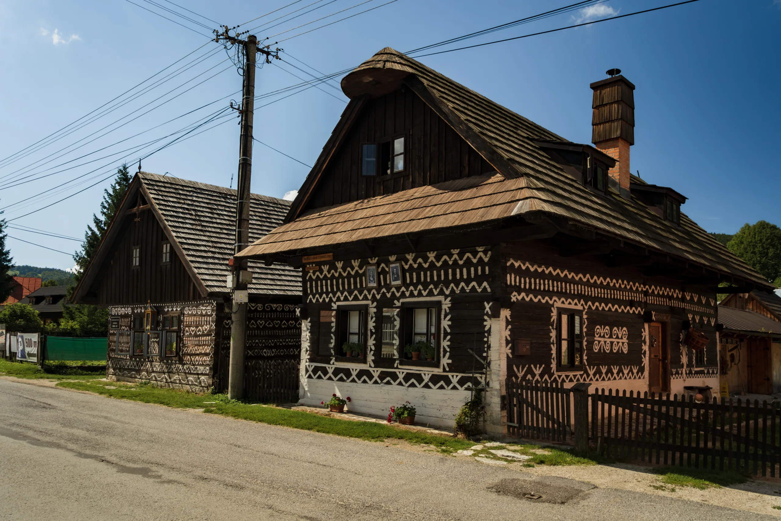 Drewniane chaty w Čičmanach na Słowacji, ozdobione tradycyjnymi białymi geometrycznymi ornamentami na ciemnych ścianach.