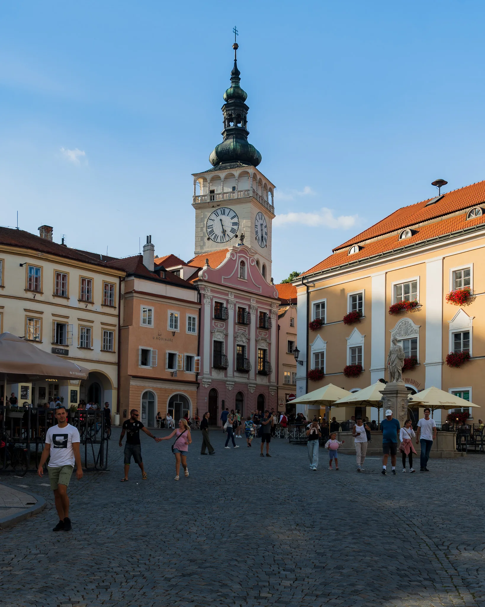Rynek w Mikulovie – kolorowe kamienice, wieża ratusza z zegarem i spacerujący ludzie w letnie popołudnie.