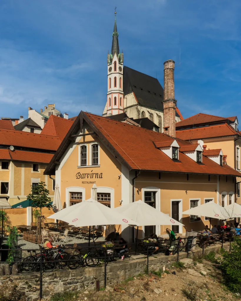 Restauracja Barvírna z ogródkiem pełnym parasoli i widokiem na wieżę kościoła św. Wita w Českým Krumlovie.