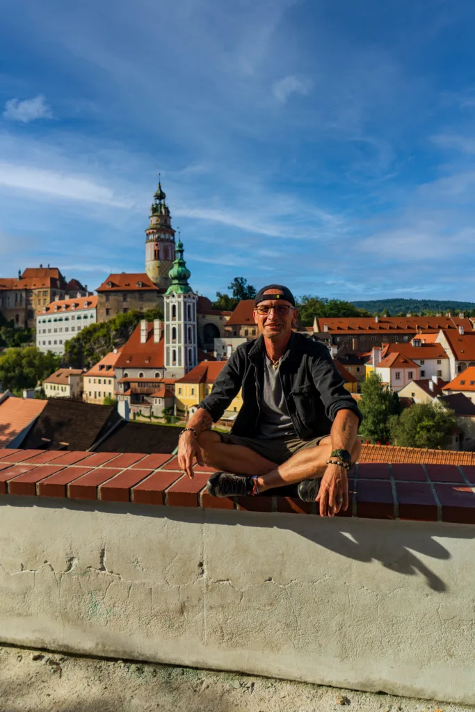 Turysta siedzi na murku z widokiem na zamek i kolorowe dachy Českého Krumlova w Czechach.