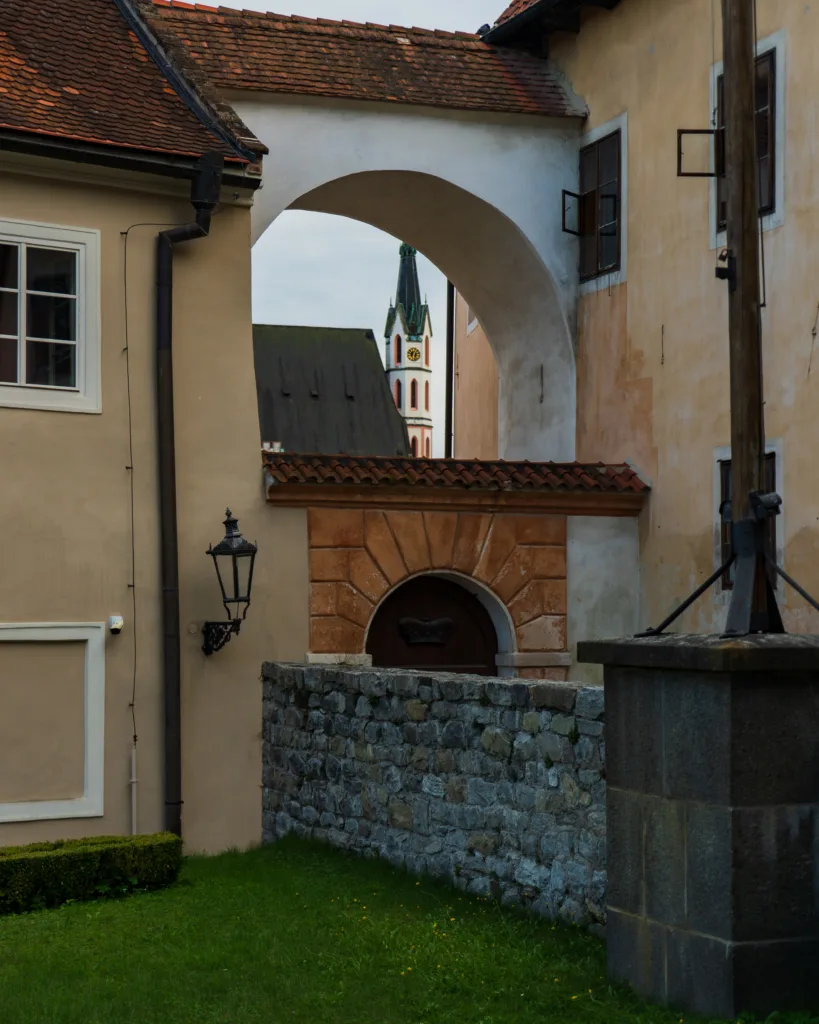 Widok na wieżę kościoła św. Wita w Českým Krumlovie przez łuk kamiennej zabudowy.