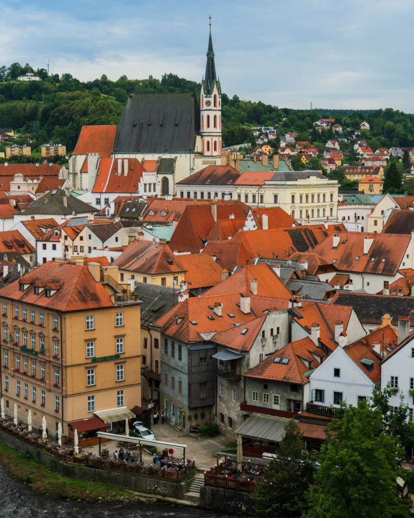 Panorama Českého Krumlova z czerwonymi dachami kamienic i dominującym kościołem św. Wita na wzgórzu.