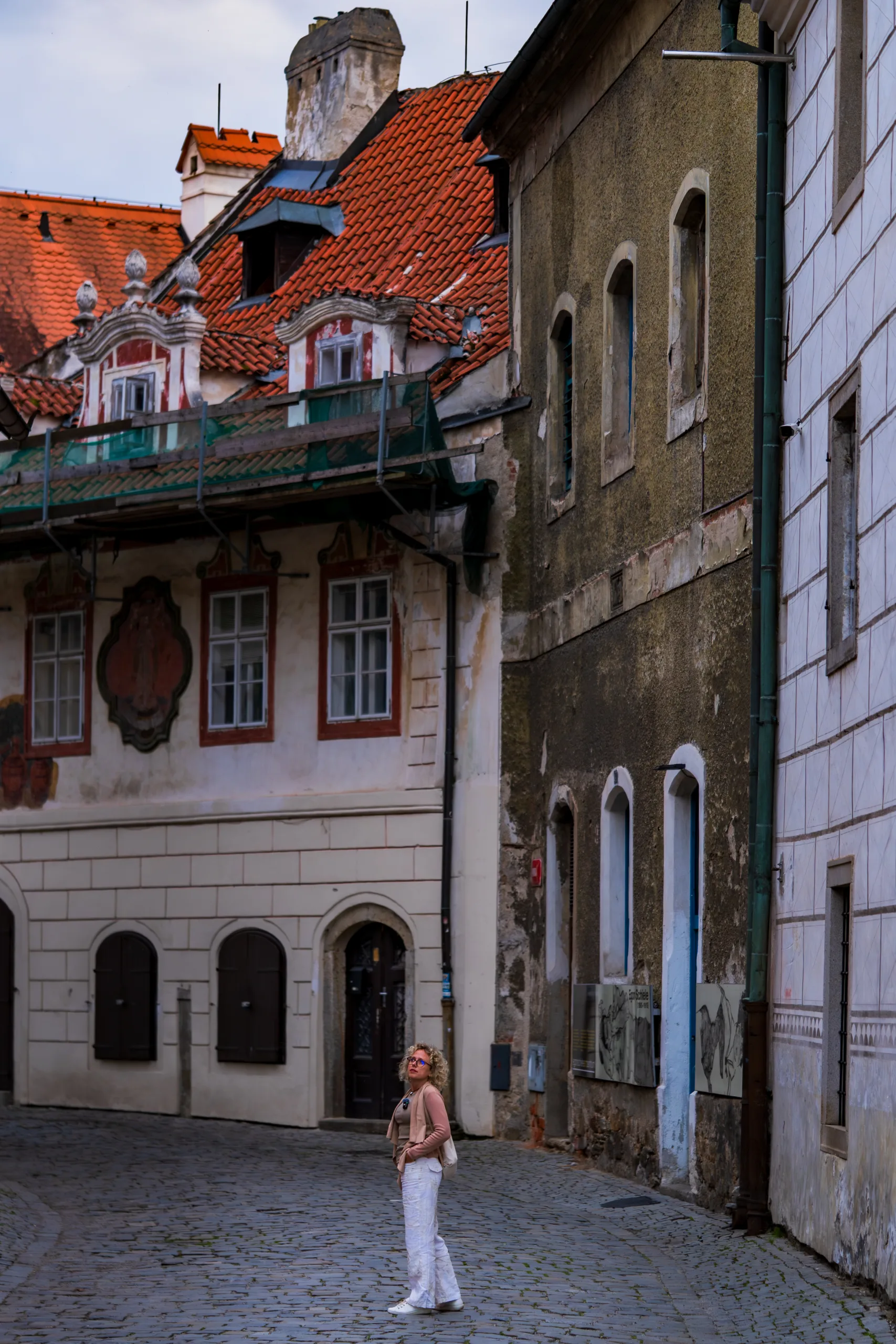 Turystka spaceruje brukowaną uliczką w Českým Krumlovie, otoczoną zabytkowymi kamienicami z czerwonymi dachami.