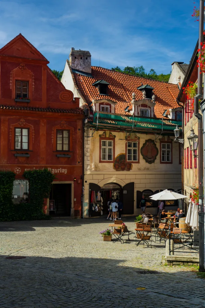 Kolorowe kamienice z czerwonymi dachami i ozdobnymi fasadami na rynku w Českým Krumlovie, z kawiarnianymi stolikami na brukowanym placu.