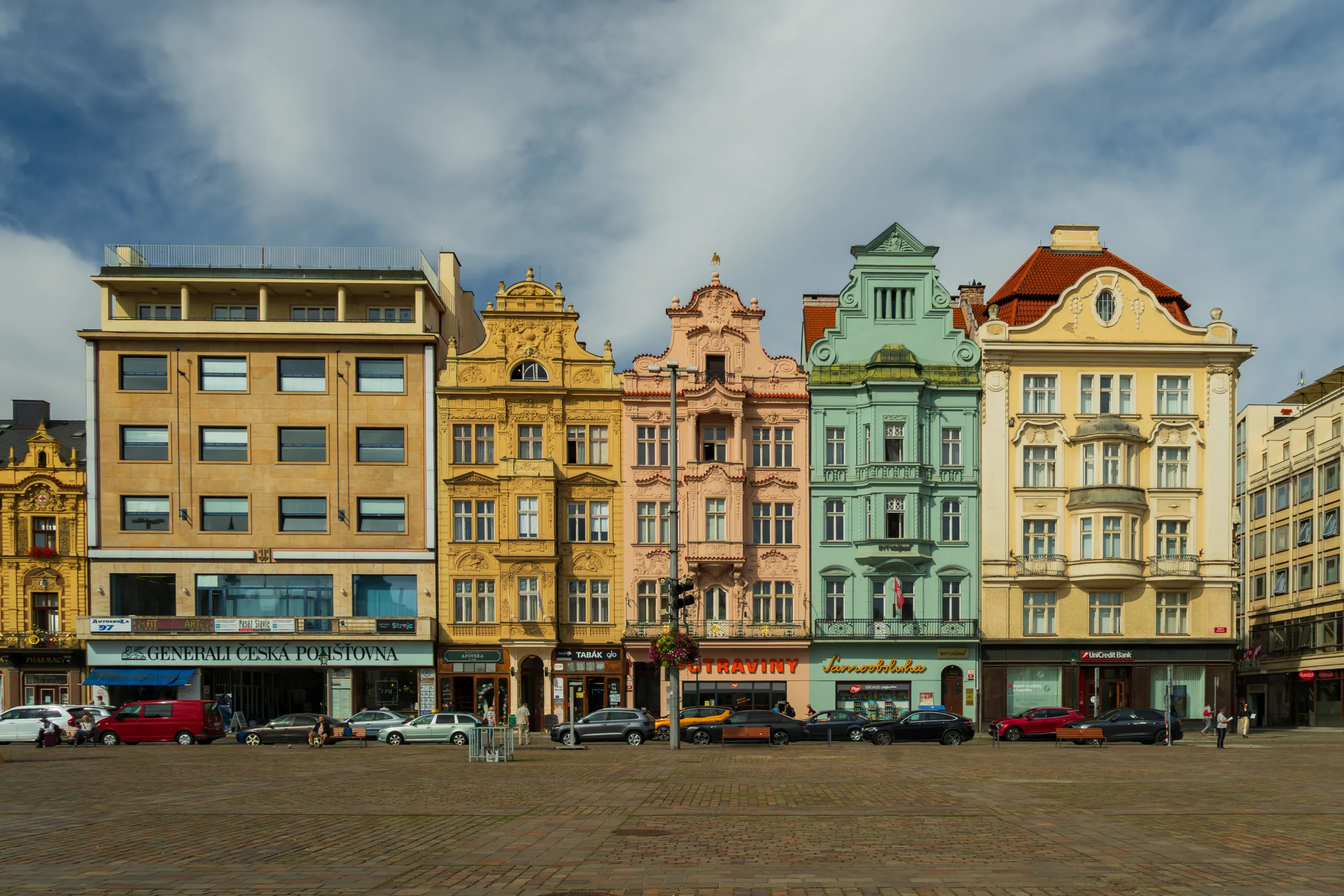 Kolorowe kamienice przy rynku w Pilznie – pastelowe fasady w odcieniach żółci, różu, zieleni i beżu obok nowoczesnego budynku.