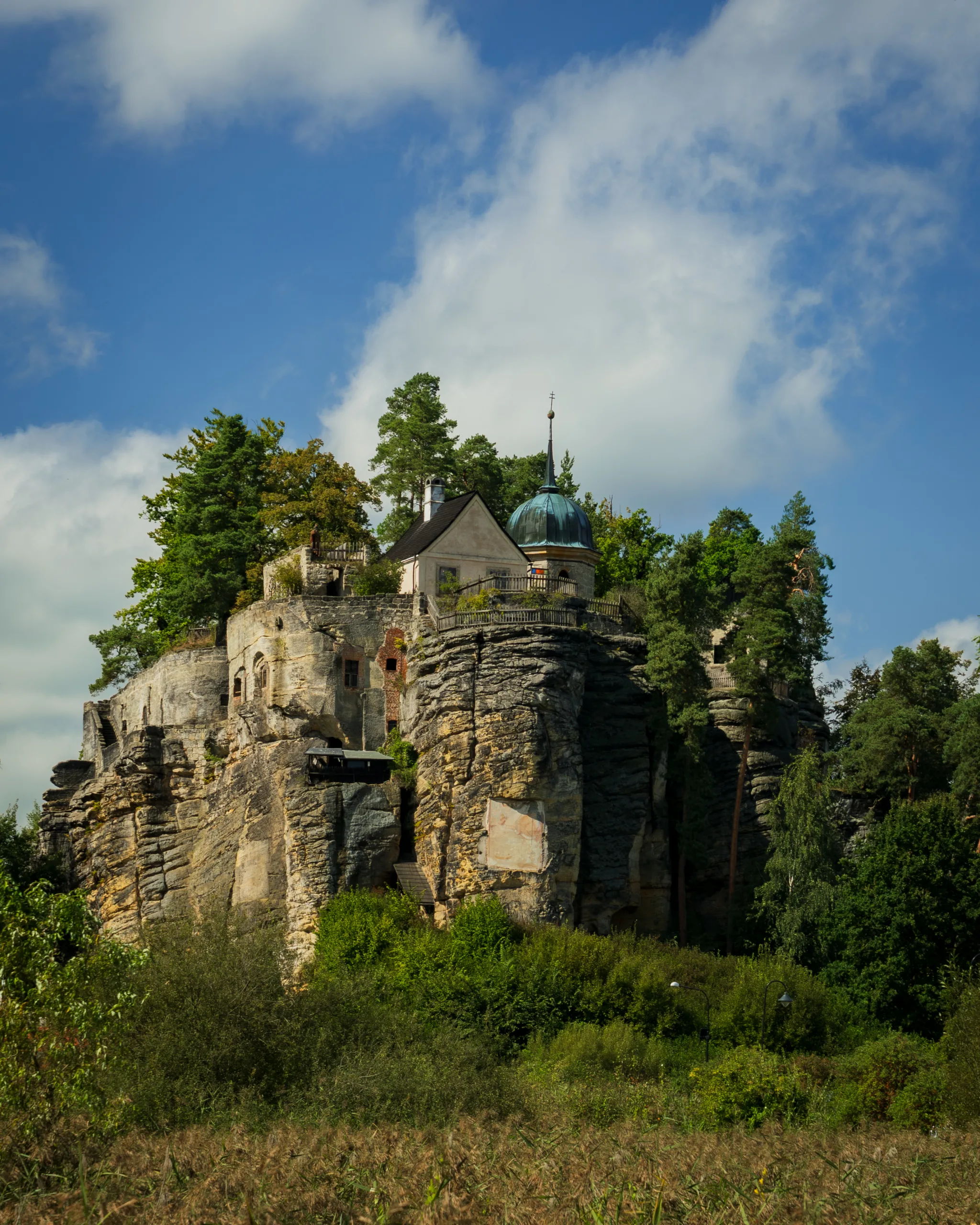 Zamek Sloup wzniesiony na potężnej skale piaskowcowej w północnych Czechach, otoczony zielenią i błękitnym niebem.