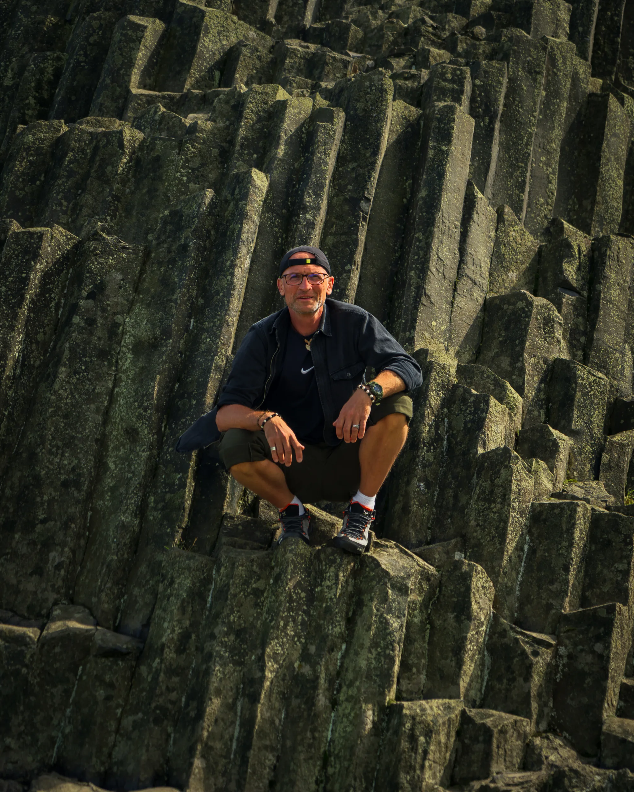 Mężczyzna siedzący na monumentalnych bazaltowych słupach skalnych Panská skála w Czechach.