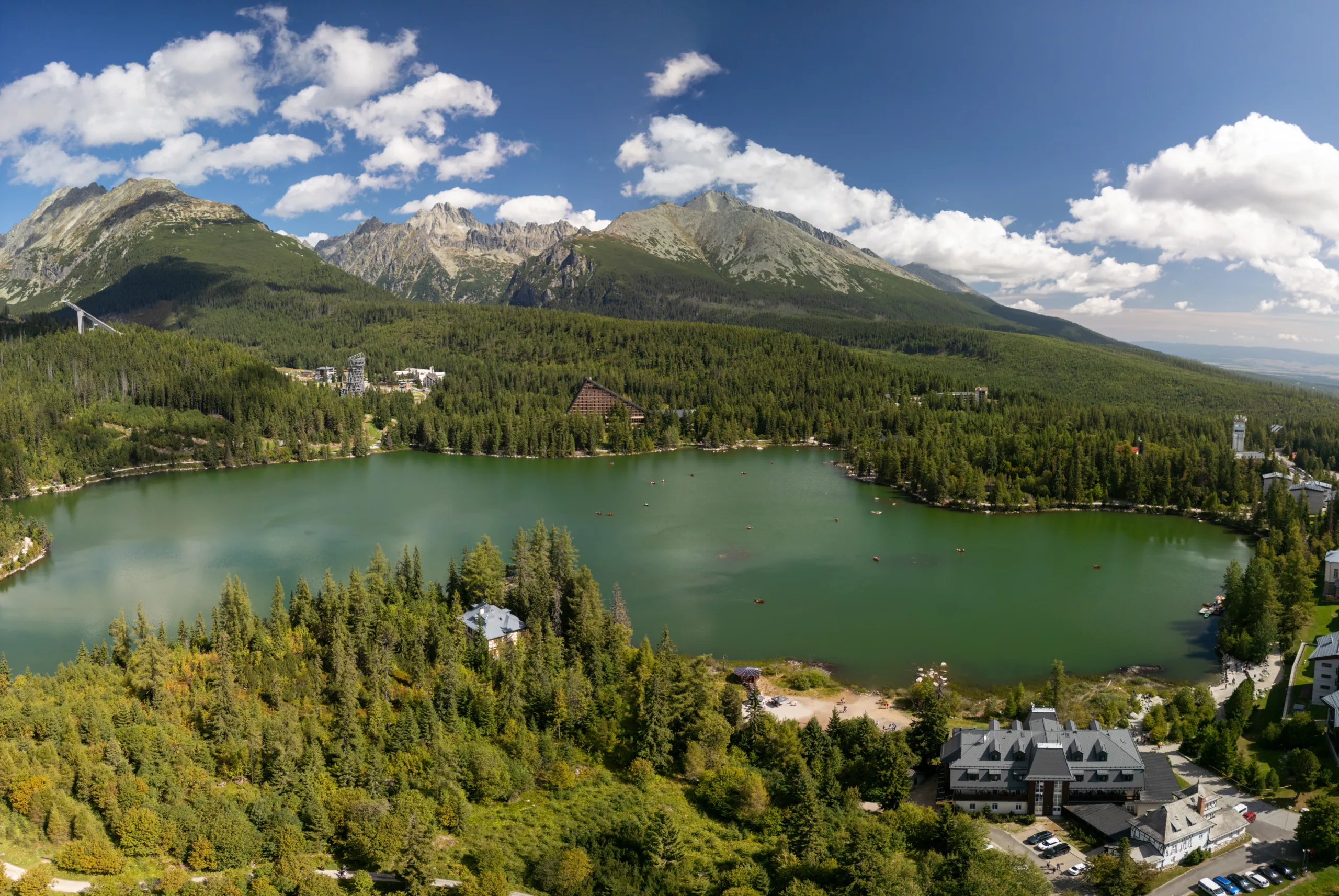 Panorama Štrbskiego Jeziora w Tatrach Wysokich na Słowacji, otoczonego lasami i górskimi szczytami.