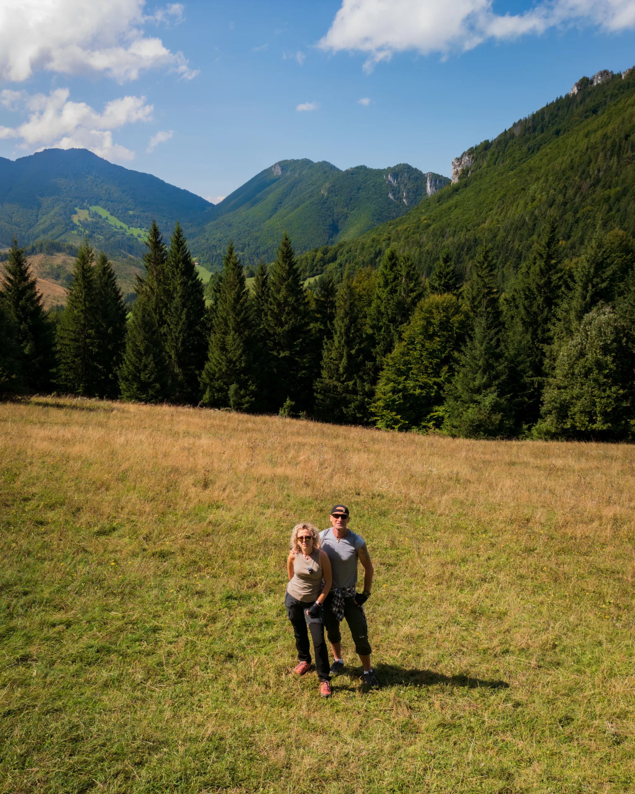 Para turystów pozuje na górskiej łące z widokiem na zalesione szczyty Wielkiej Fatry. Janosikove Diery - Mała Fatra