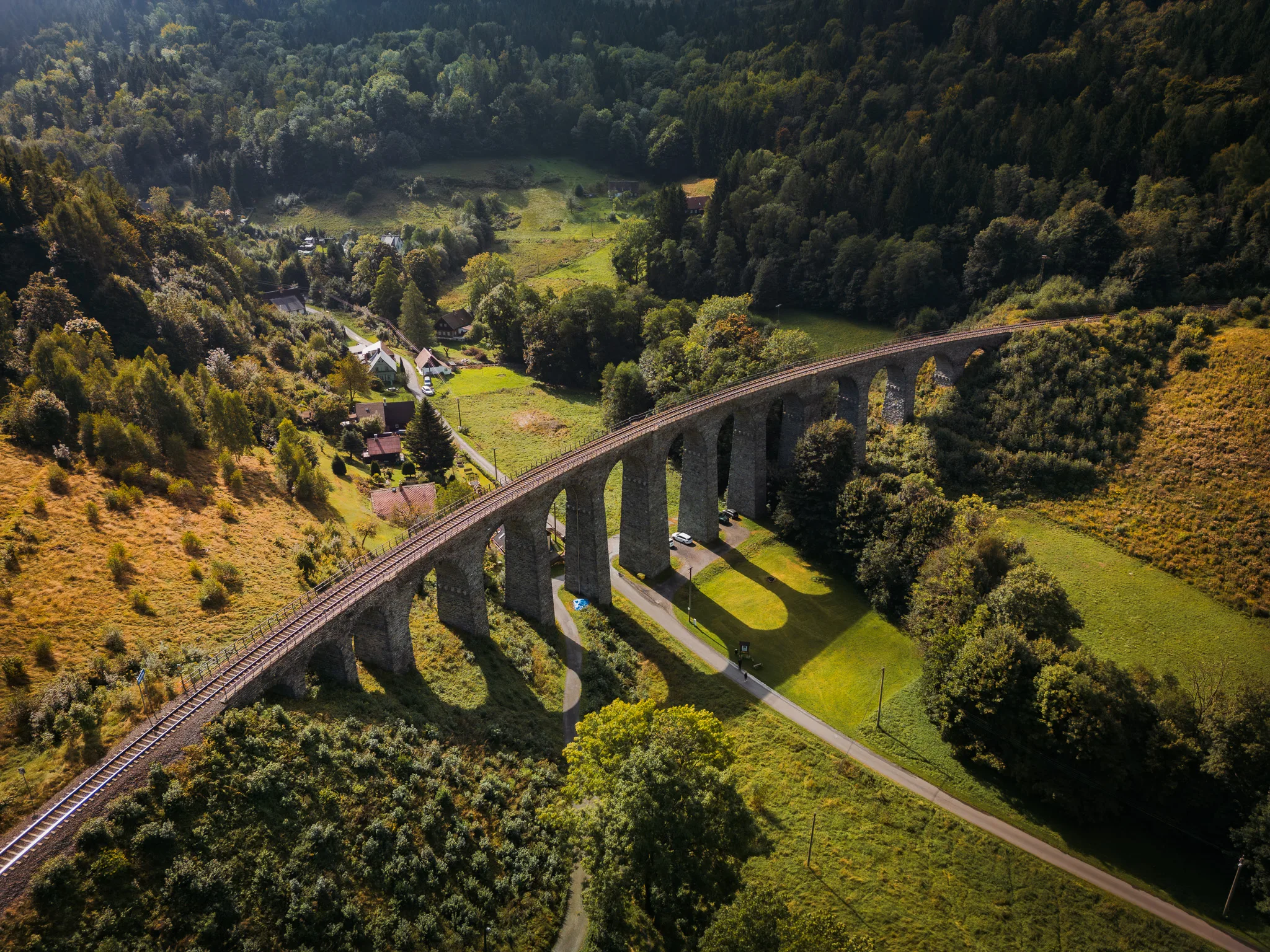 Malowniczy kamienny wiadukt kolejowy w Czeskim Raju, rozciągający się nad zieloną doliną i otoczony lasami.