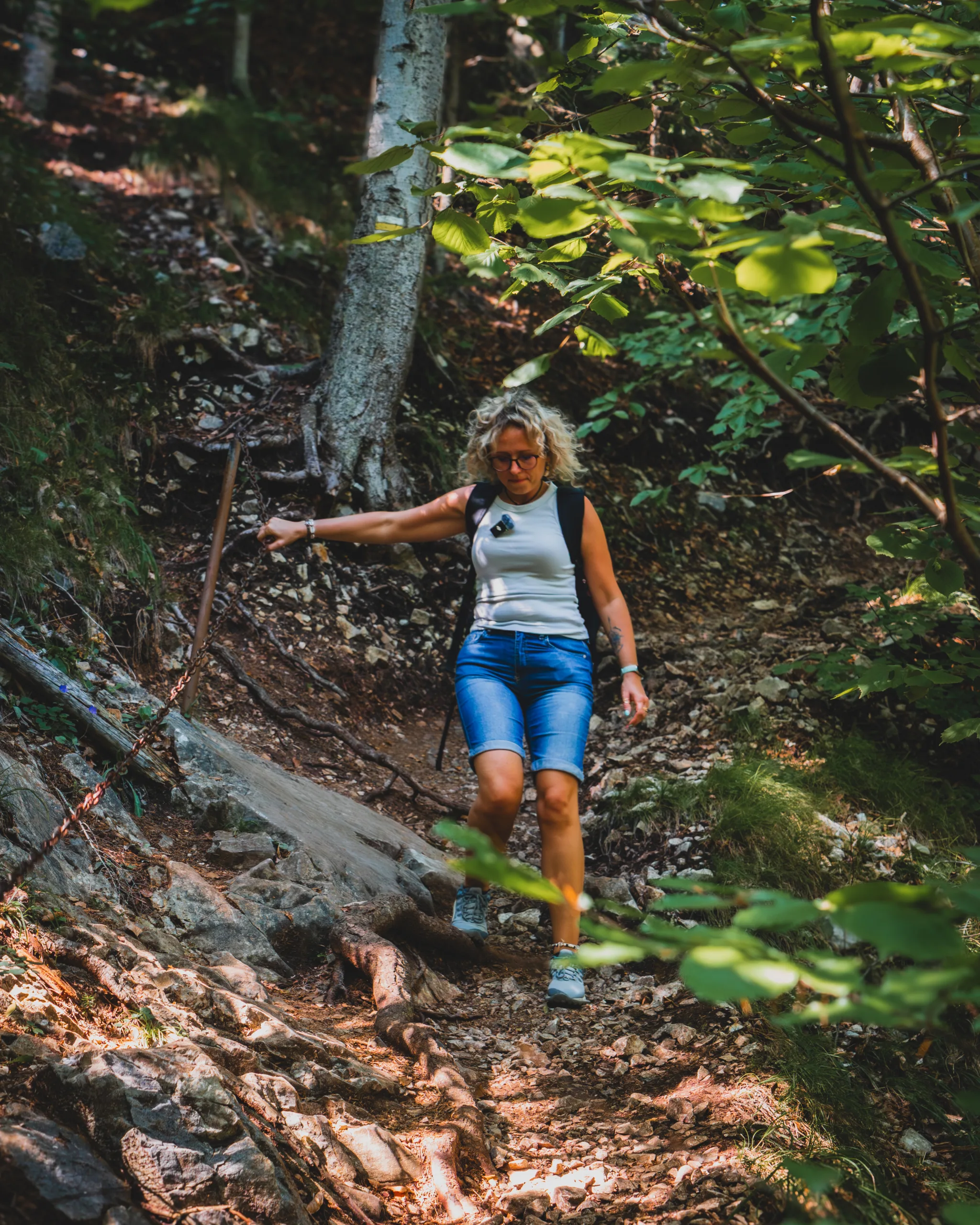 Turystka schodząca stromym leśnym szlakiem w Słowackim Raju, w otoczeniu drzew i korzeni.