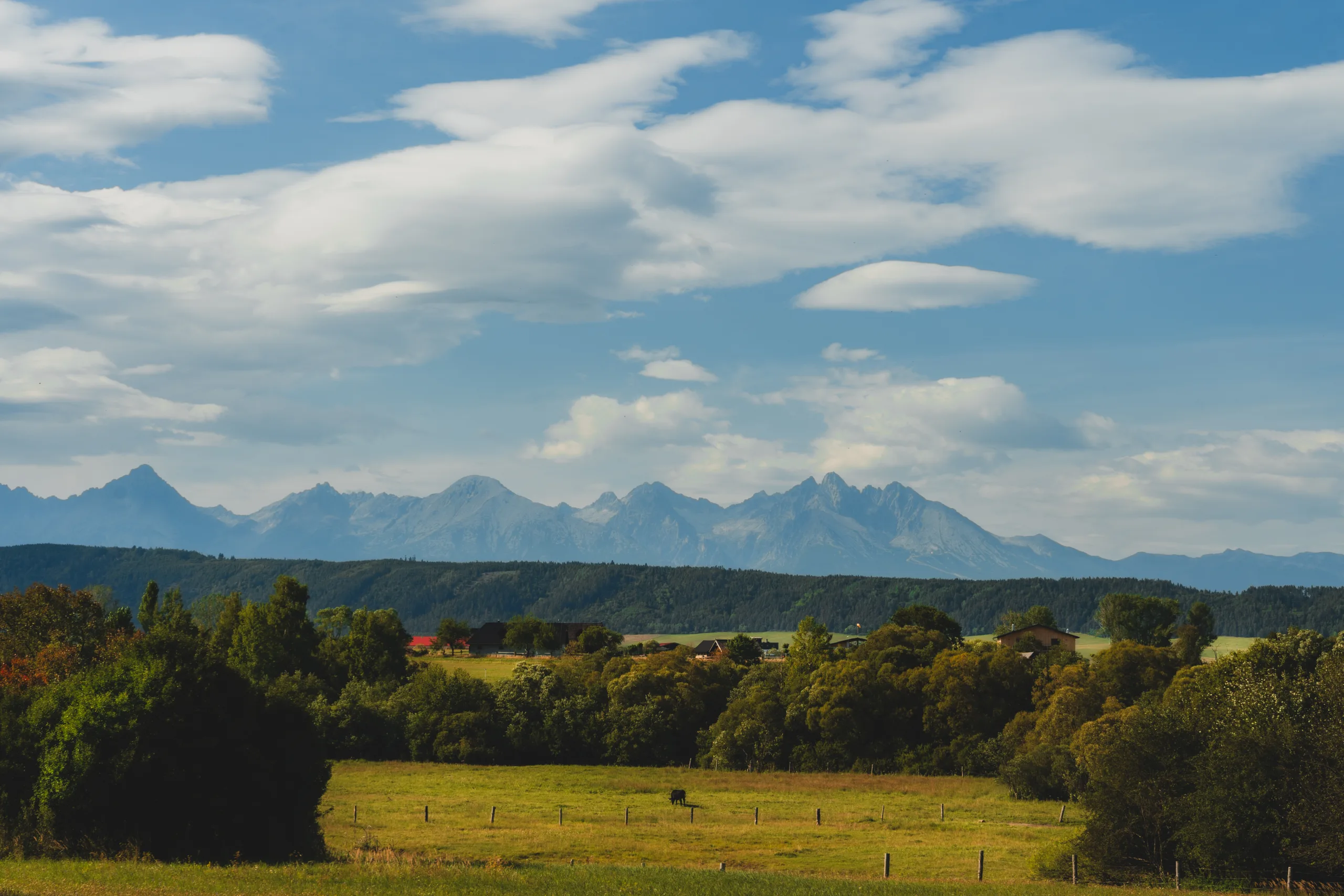 Panorama Tatr widziana z okolic Słowackiego Raju – zielone pola, lasy i majestatyczne szczyty gór w oddali.