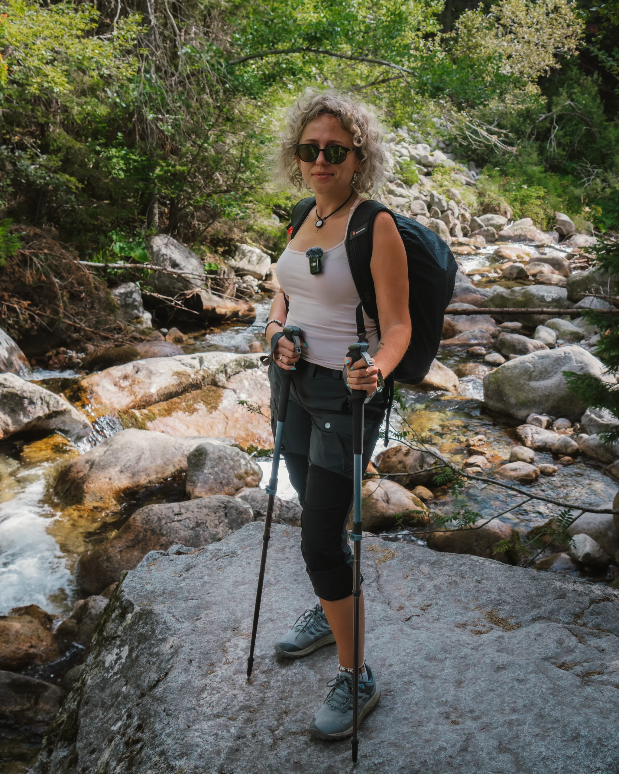 Turystka z kijkami trekkingowymi stojąca na skale nad górskim potokiem w Tatrach Wysokich.