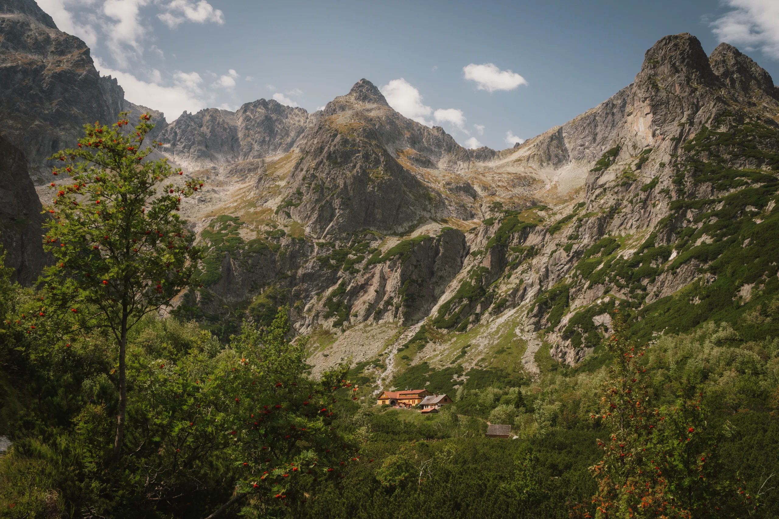 Widok na górskie schronisko położone w dolinie Tatr Wysokich, otoczone stromymi szczytami i zielenią kosodrzewiny - Zielony Staw Kieżmarski 