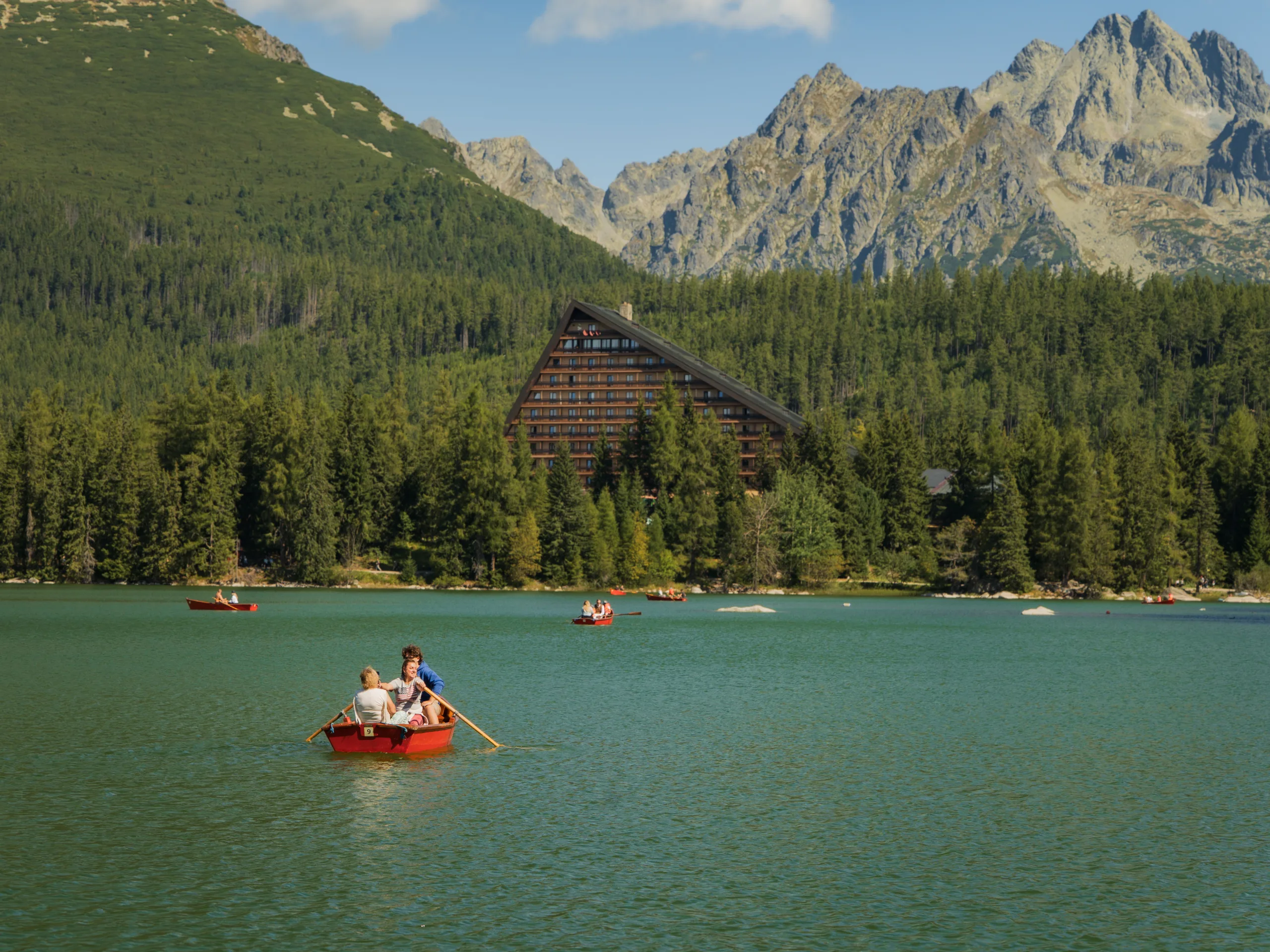 Czerwone łódki na Štrbskim Jeziorze w Tatrach Wysokich, z widokiem na hotel Patria i górskie szczyty w tle - Szczyrbskie Jezioro.