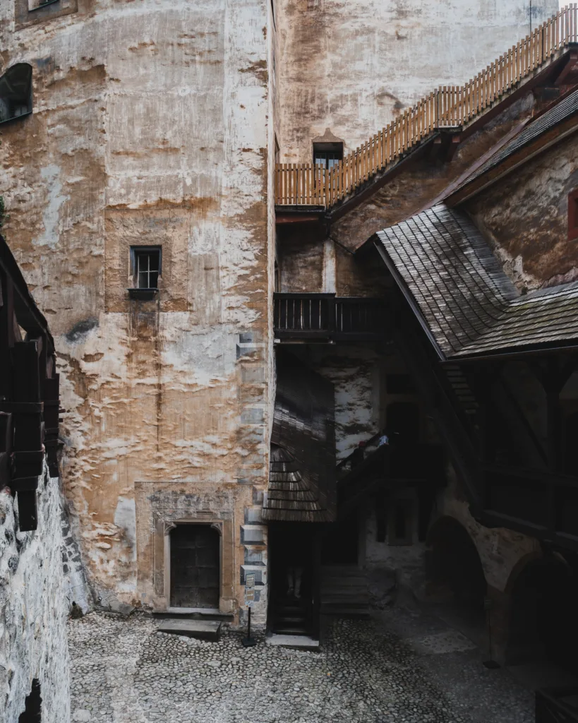 Dziedziniec Zamku Orawskiego na Słowacji z kamiennym brukiem, starymi murami i drewnianymi schodami prowadzącymi na wyższe kondygnacje.