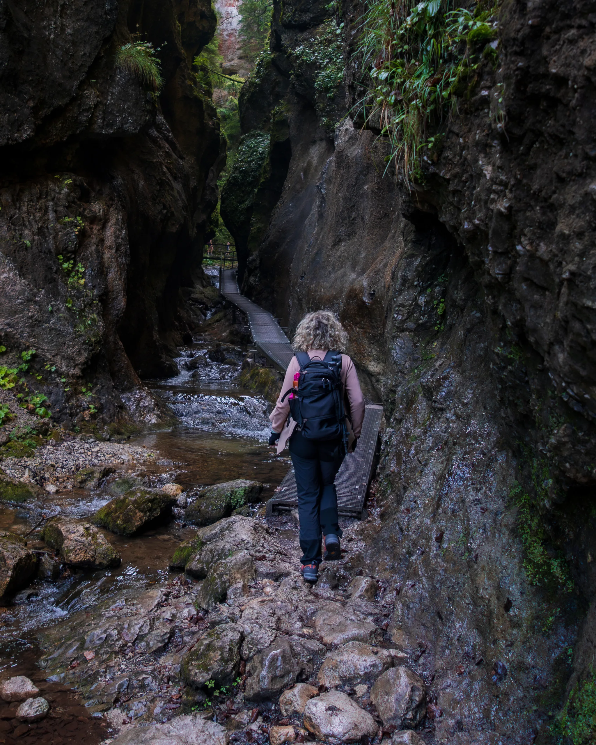 Turystka na szlaku Jánošíkowe Diery w Małej Fatrze, idąca wąwozem wśród skalnych ścian i potoku.