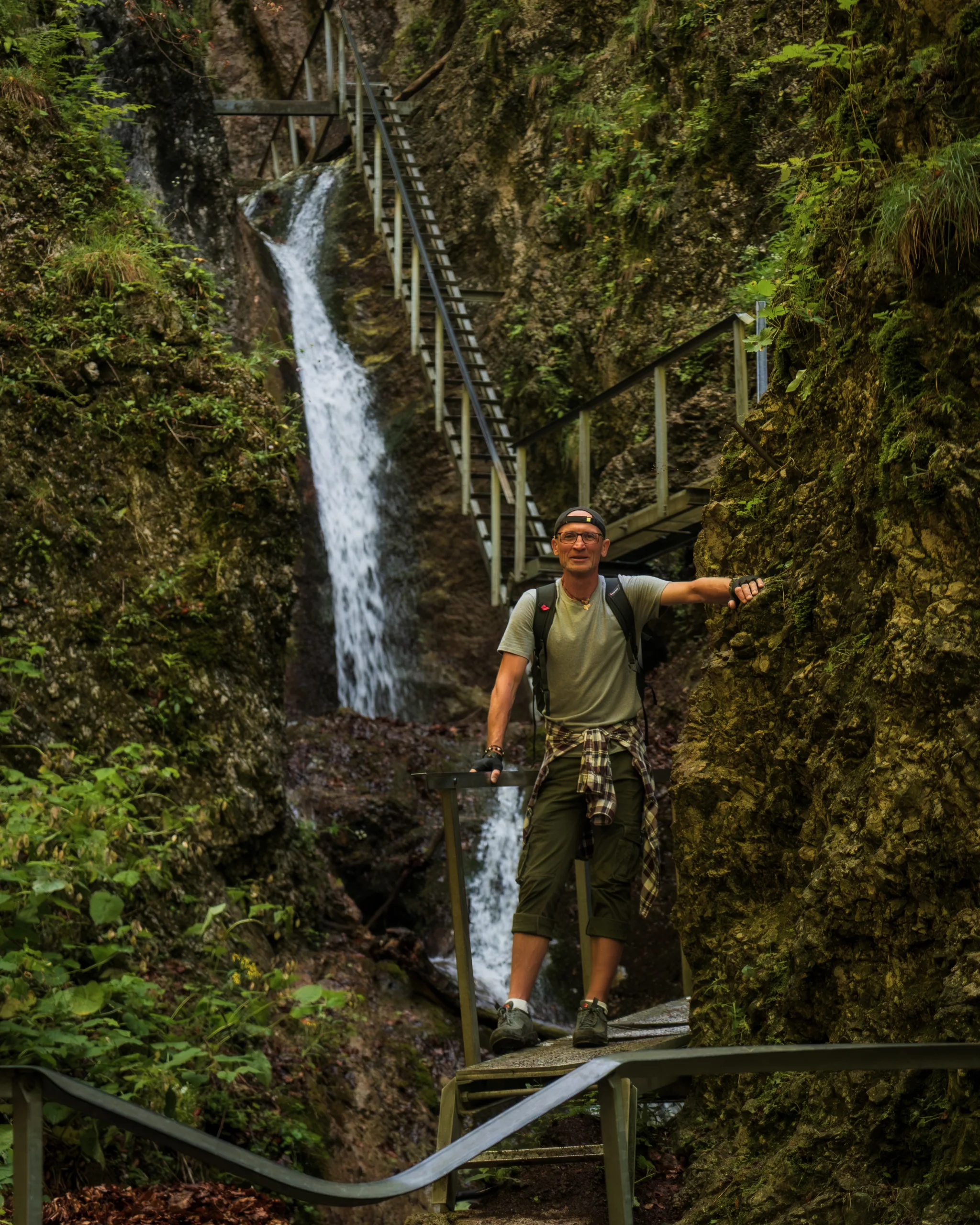 Turysta na metalowej kładce przy wodospadzie w wąwozie podczas trekkingu w Małej Fatrze.