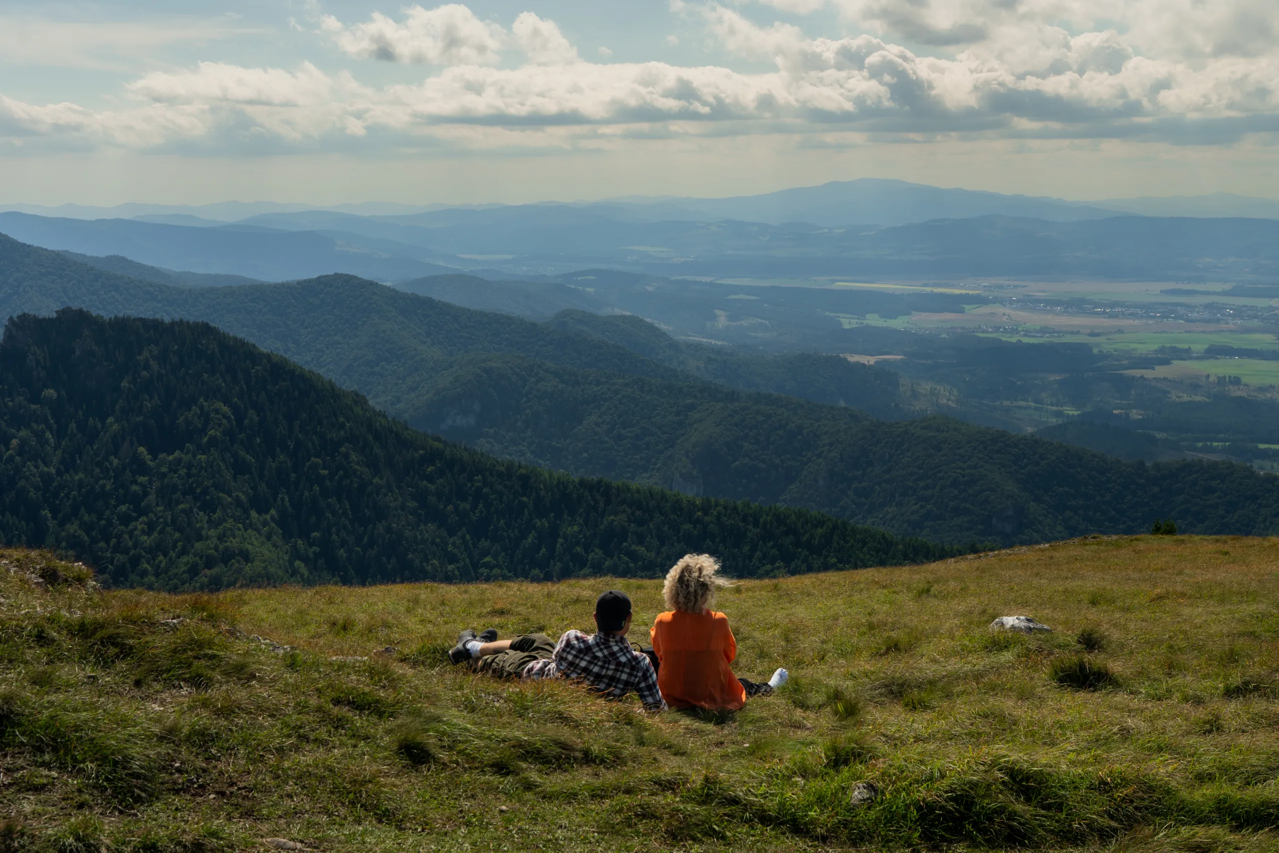 Para turystów odpoczywająca na trawie na szczycie Wielkiej Fatry z rozległym widokiem na górskie pasma i doliny Słowacji. - wielka fatra