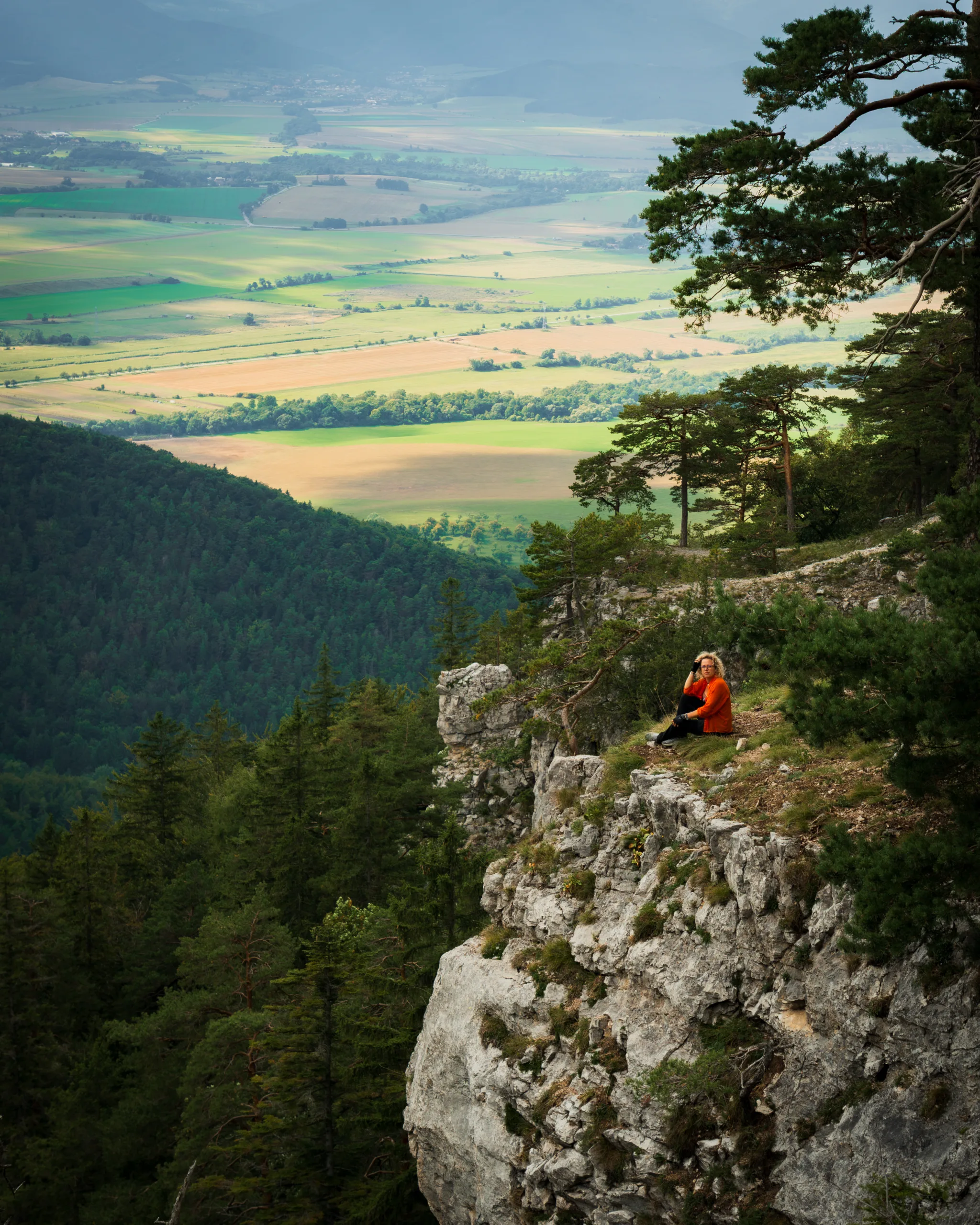 Kobieta w pomarańczowym swetrze siedząca na skalnej krawędzi z widokiem na dolinę i las w Wielkiej Fatrze.