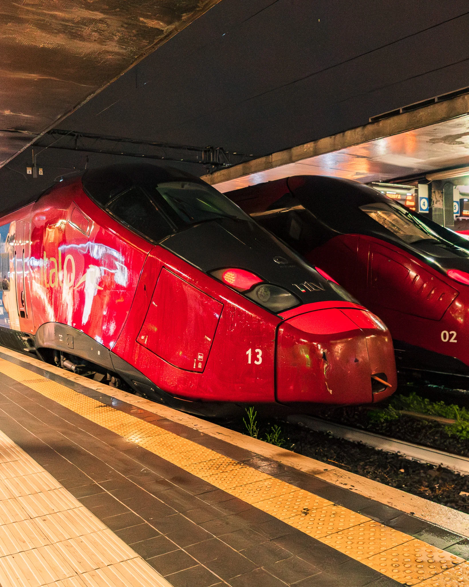 Czerwone pociągi dużych prędkości Italo stojące na peronie we włoskim dworcu kolejowym.