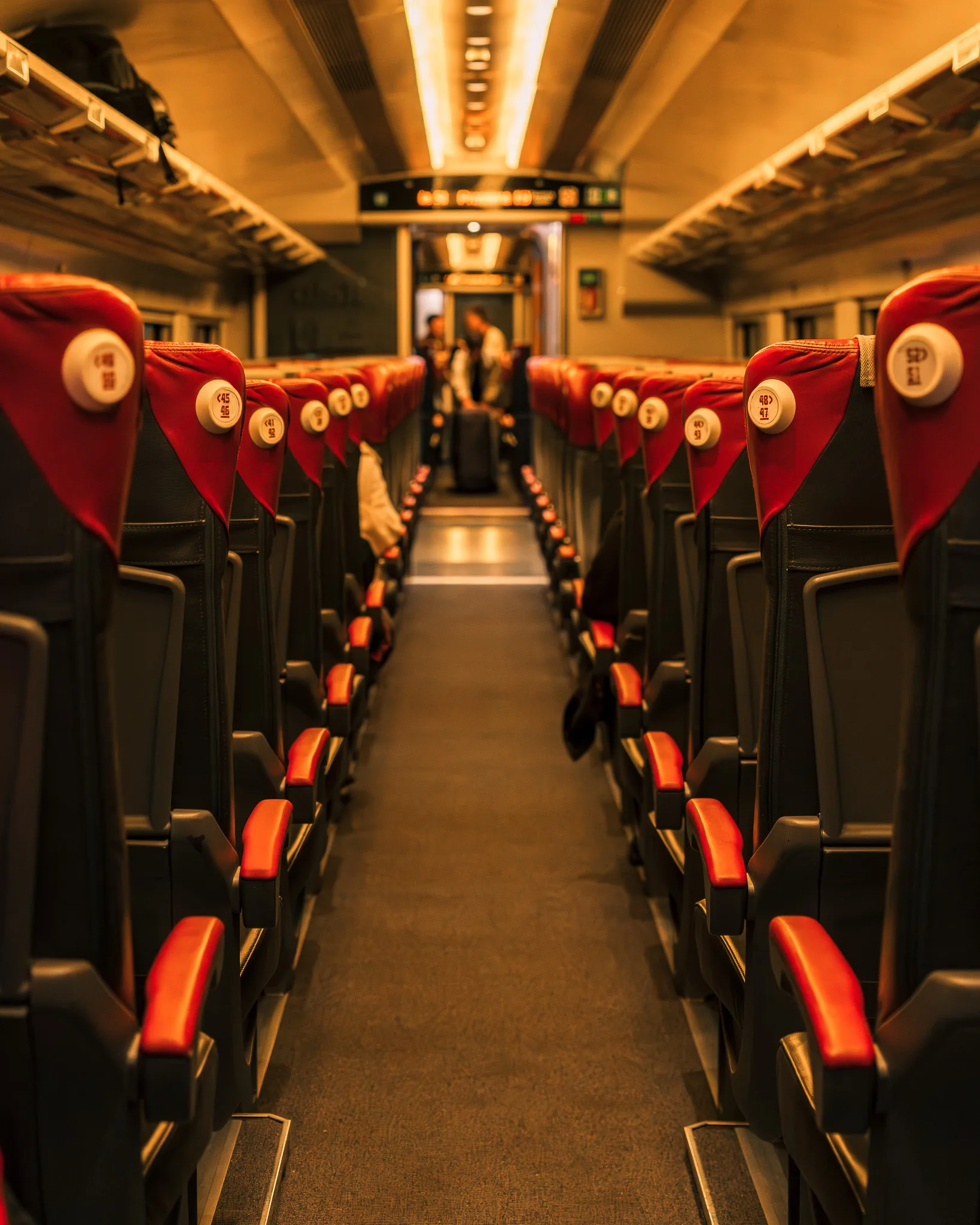 Wnętrze nowoczesnego pociągu Italo we Włoszech z czerwonymi siedzeniami i oświetleniem w ciepłych barwach.