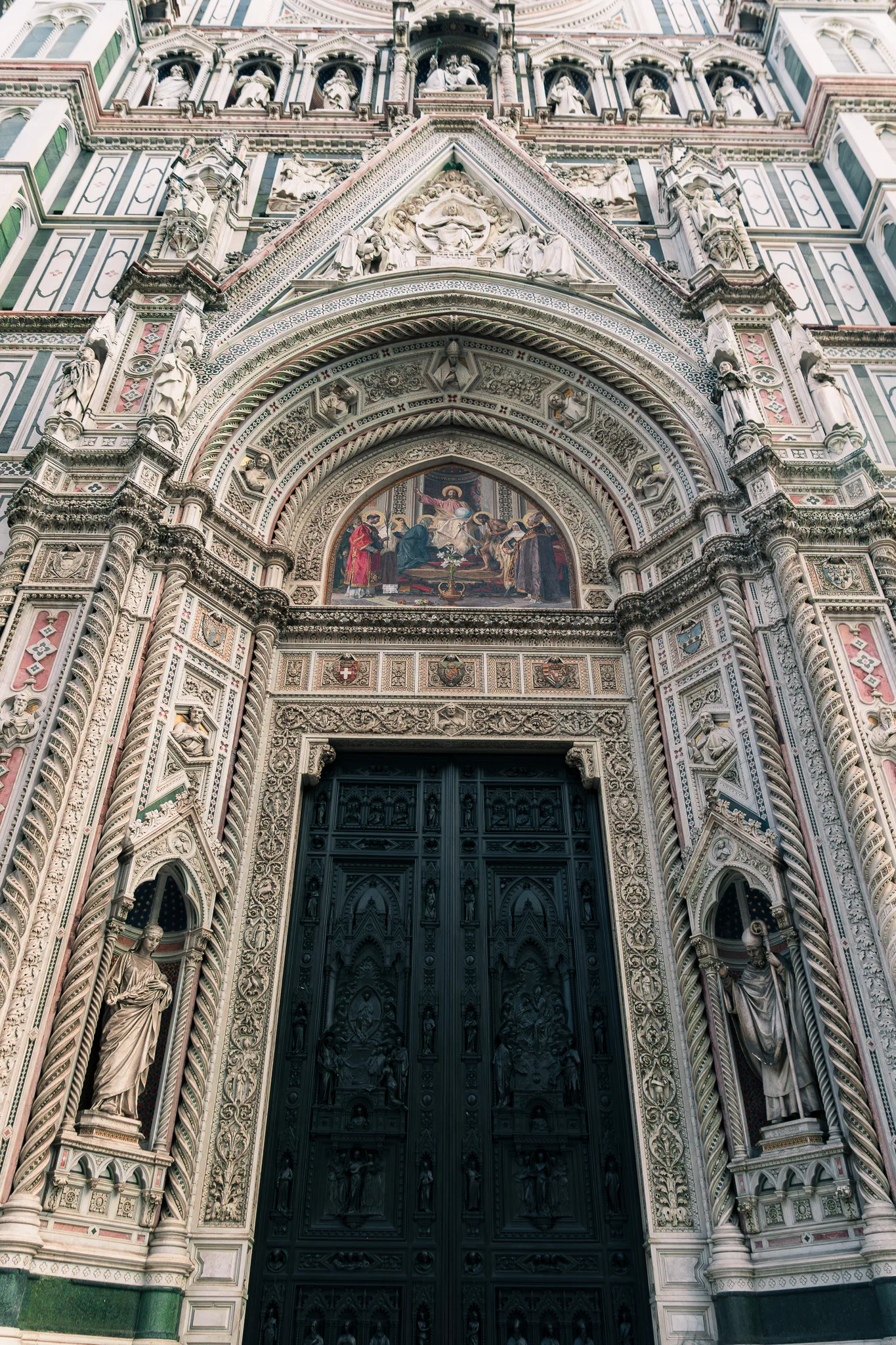 Bogato zdobione wejście do Katedry Santa Maria del Fiore we Florencji z rzeźbami, mozaiką i detalami w marmurze.