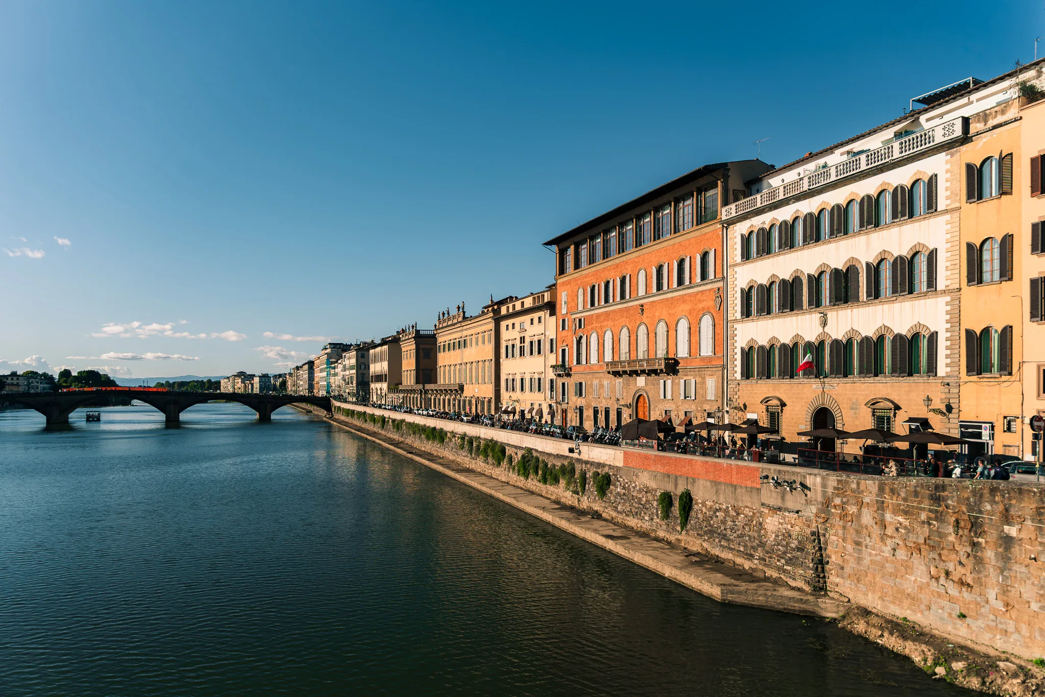 Promenada nad rzeką Arno we Florencji z kolorowymi kamienicami oświetlonymi popołudniowym słońcem.