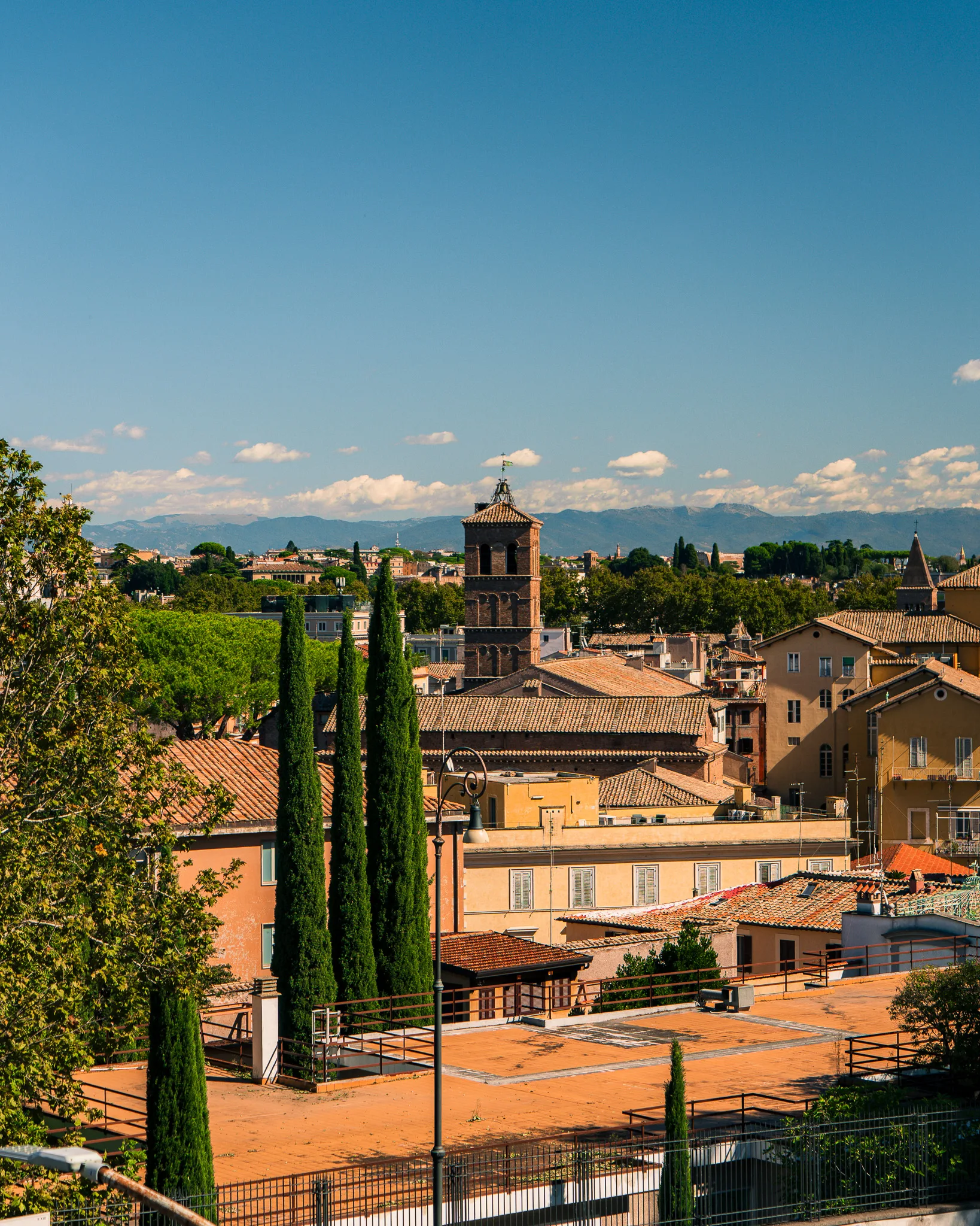 Panorama Rzymu z widokiem na dachy kamienic i ceglany dzwonnicę w dzielnicy Trastevere w słoneczny dzień.
