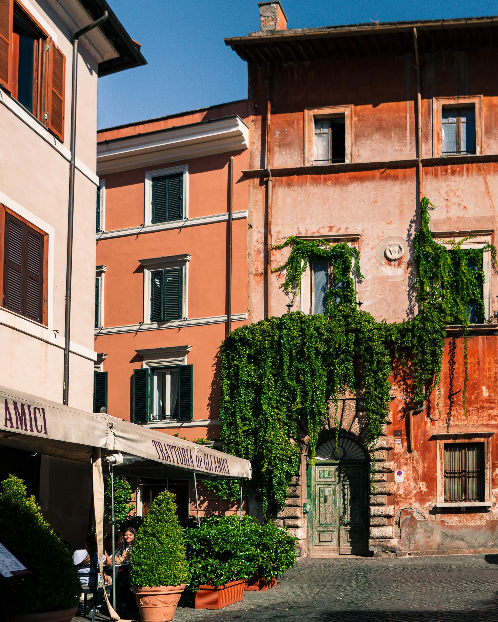 Urokliwa uliczka w dzielnicy Trastevere w Rzymie z restauracją Trattoria de Gli Amici i starymi kamienicami porośniętymi winoroślą.