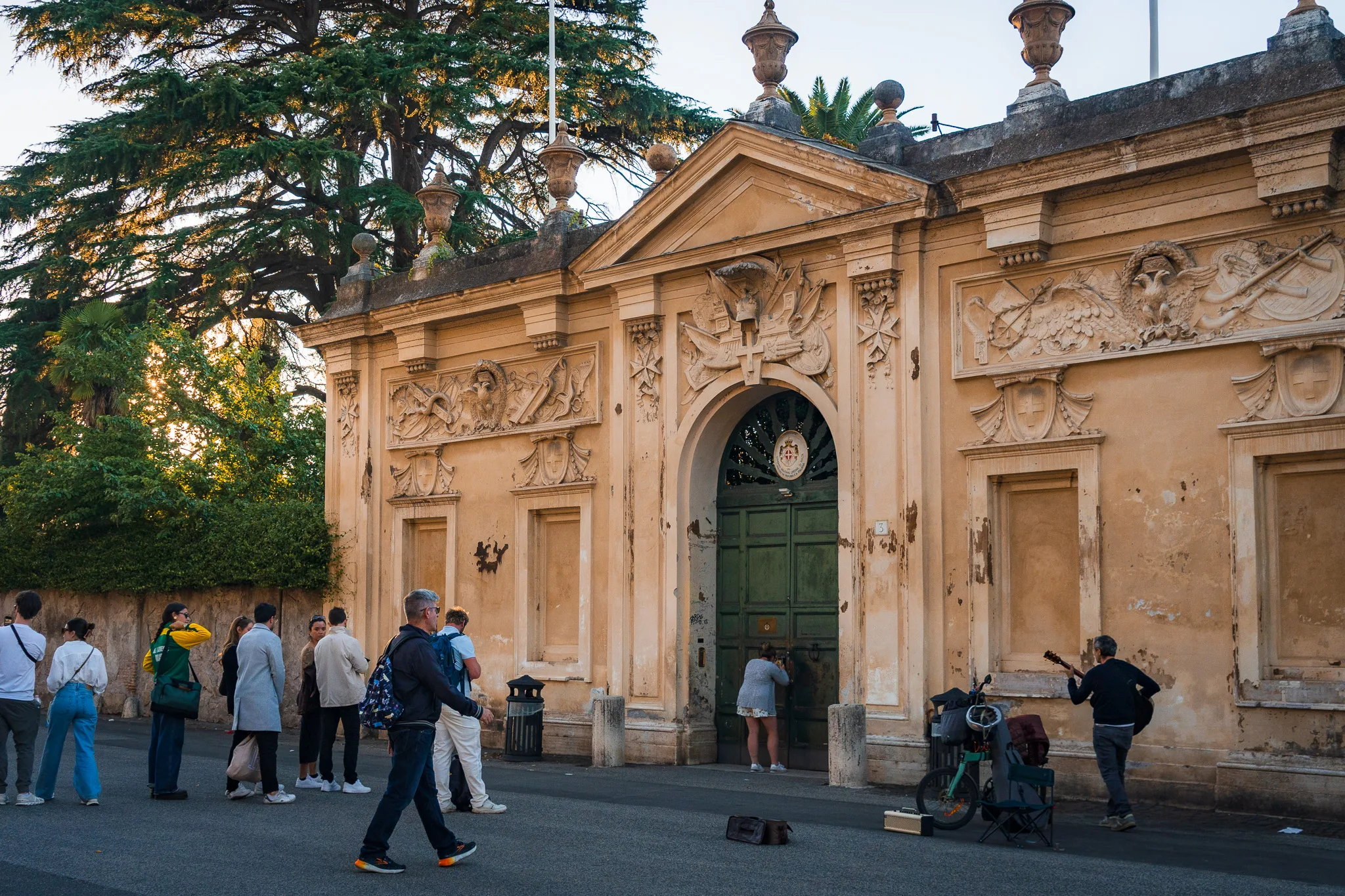 Wejście do Ogrodu Kawalerów Maltańskich w Rzymie, z ludźmi stojącymi w kolejce do słynnego dziurki od klucza