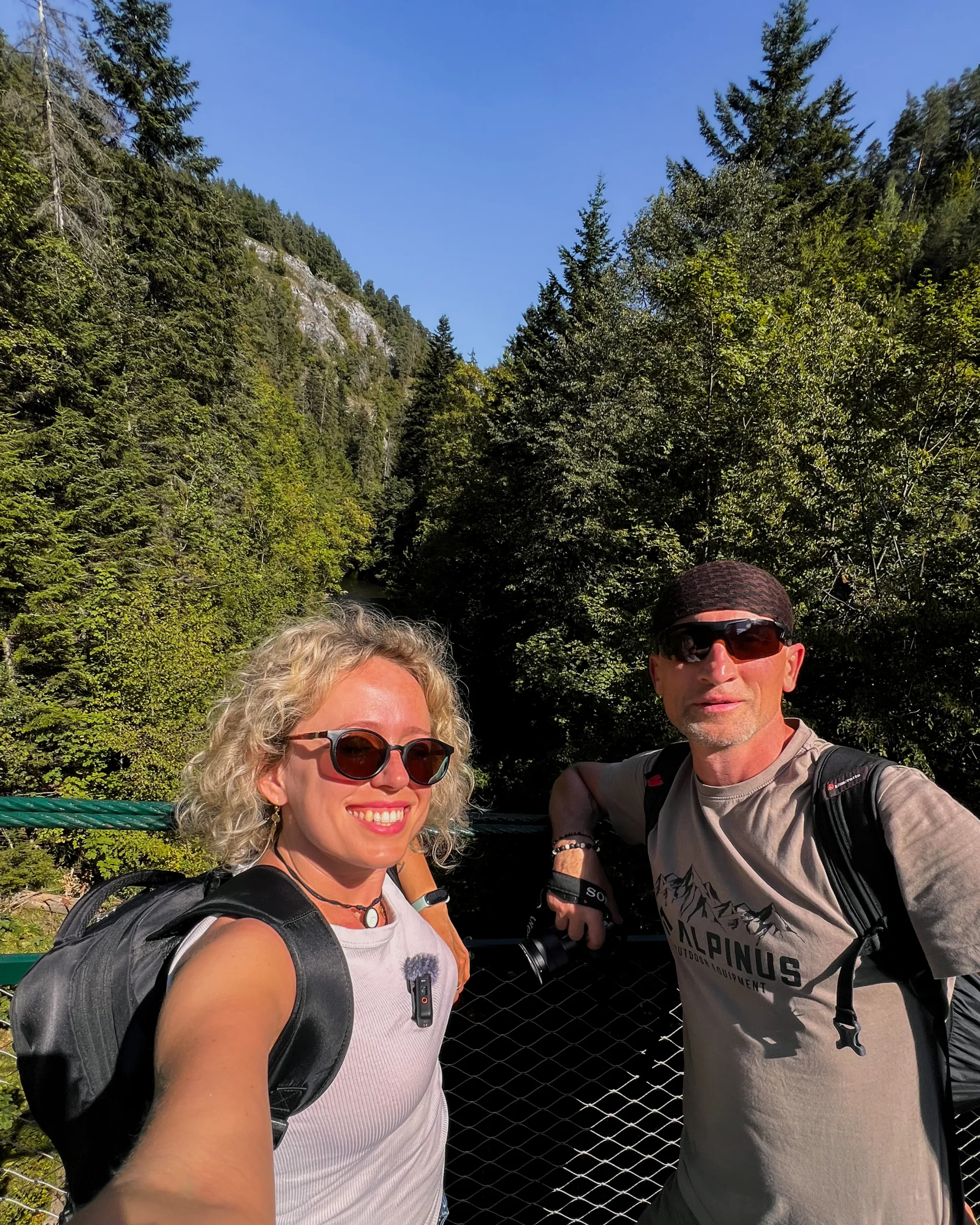 Para turystów na moście w Słowackim Raju, otoczona zielonym lasem i skalistymi zboczami w słoneczny dzień.