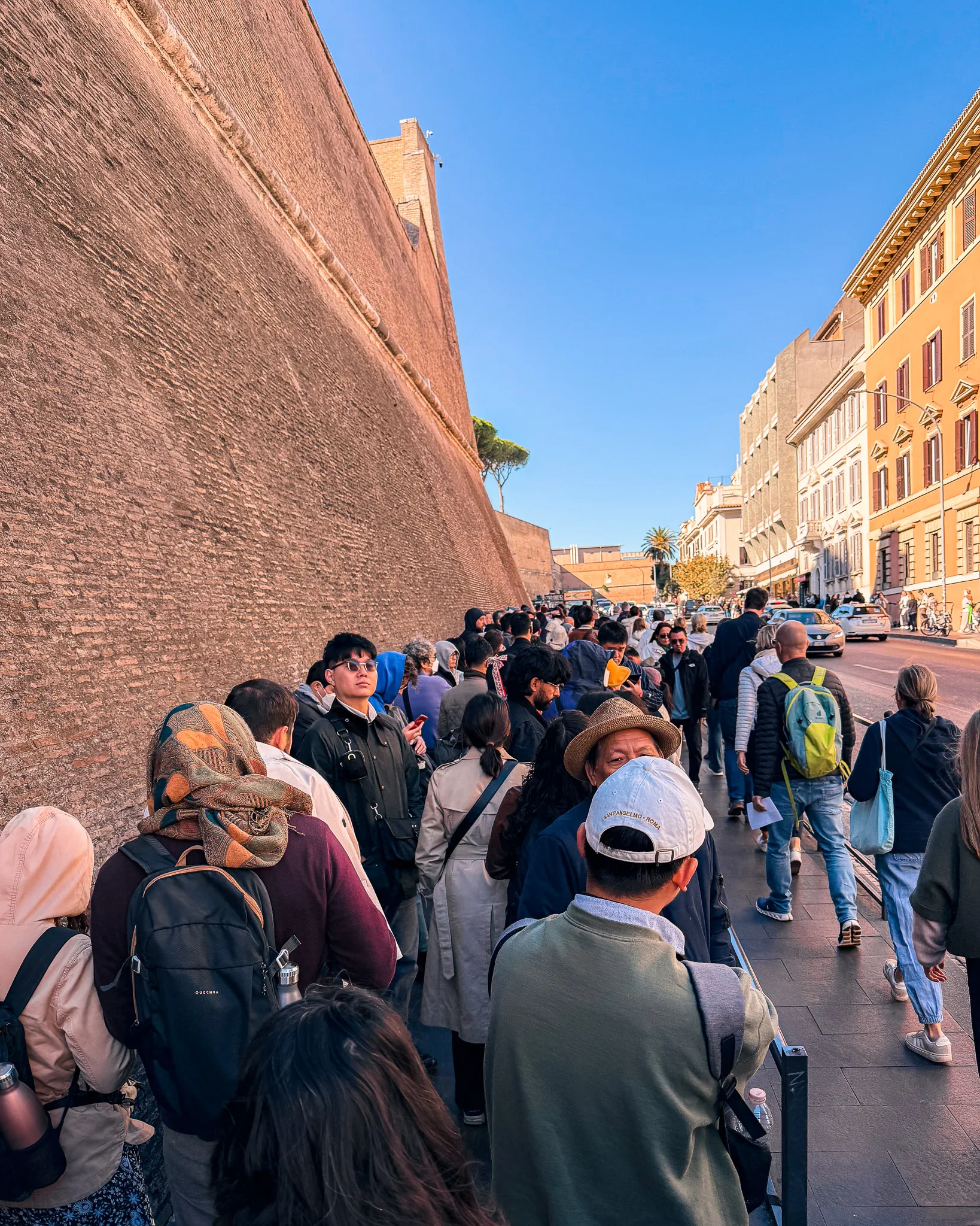 Turyści stojący w długiej kolejce wzdłuż muru Watykanu w oczekiwaniu na wejście do Muzeów Watykańskich.