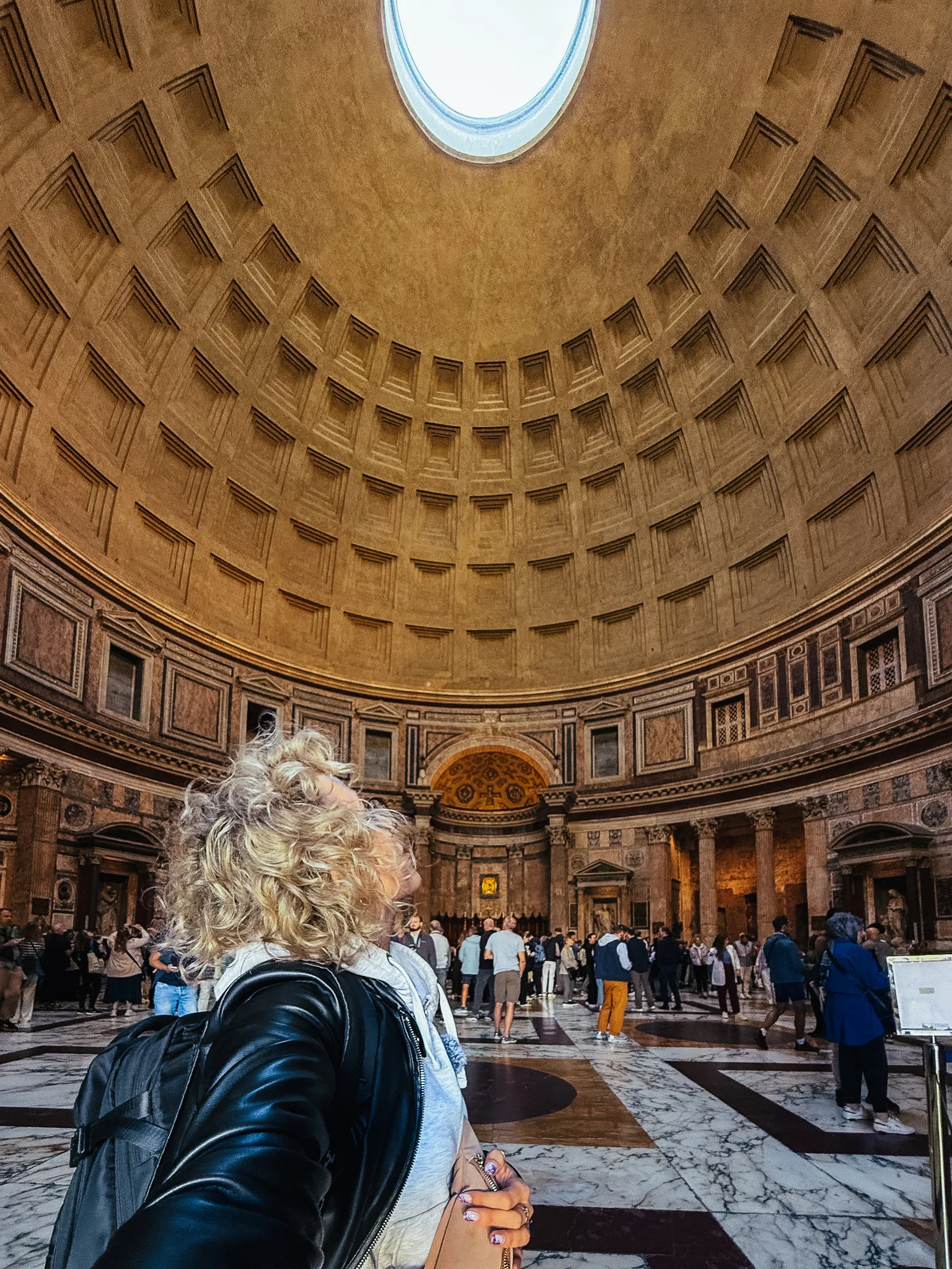 Wnętrze Panteonu w Rzymie z kopułą i oculusem, przez który wpada światło, oraz turystką podziwiającą architekturę.