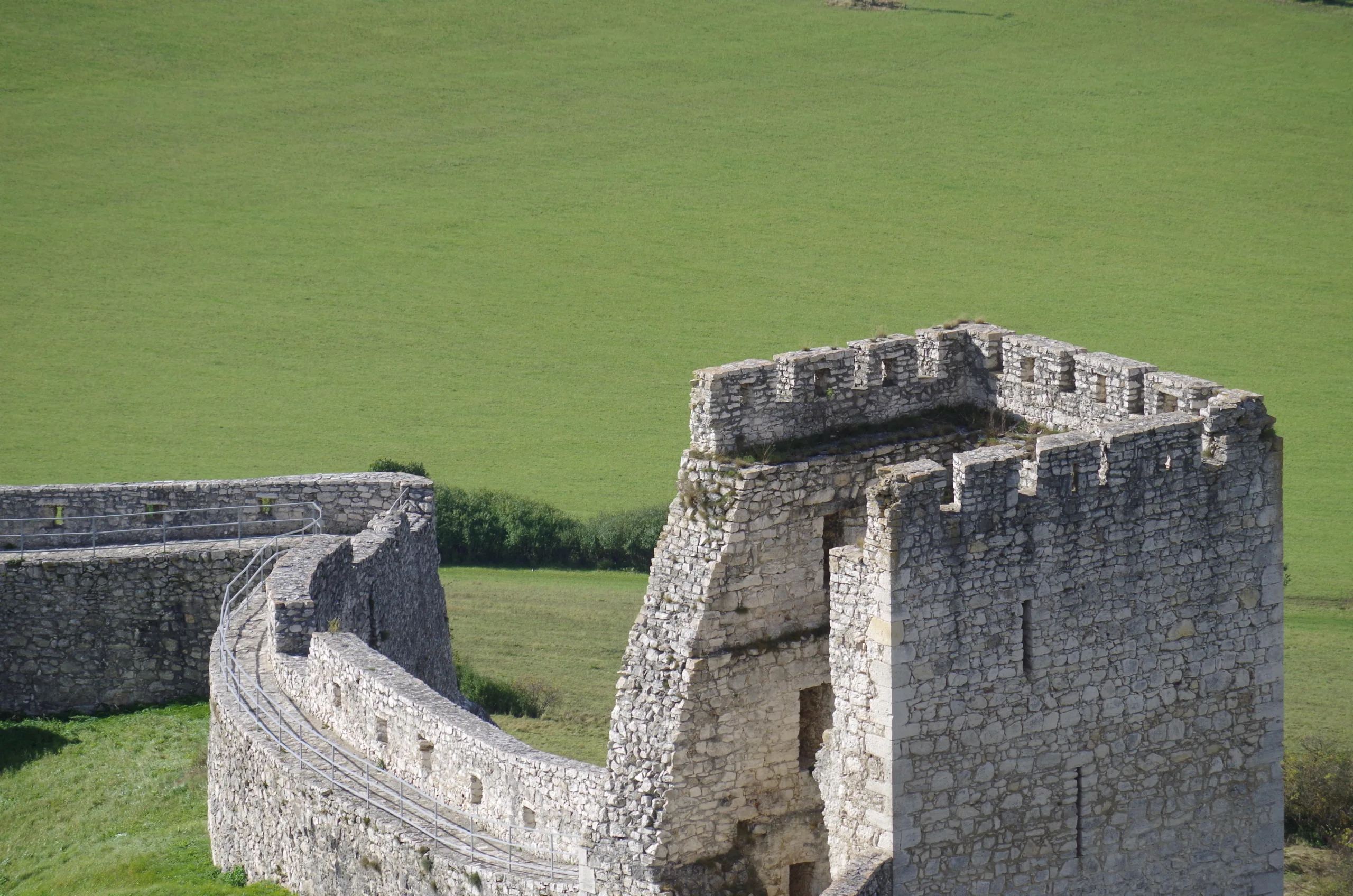 Fragment murów obronnych i baszty Zamku Spiskiego na Słowacji, widok na kamienne fortyfikacje otoczone zielonymi polami - Zamki na Słowacji
