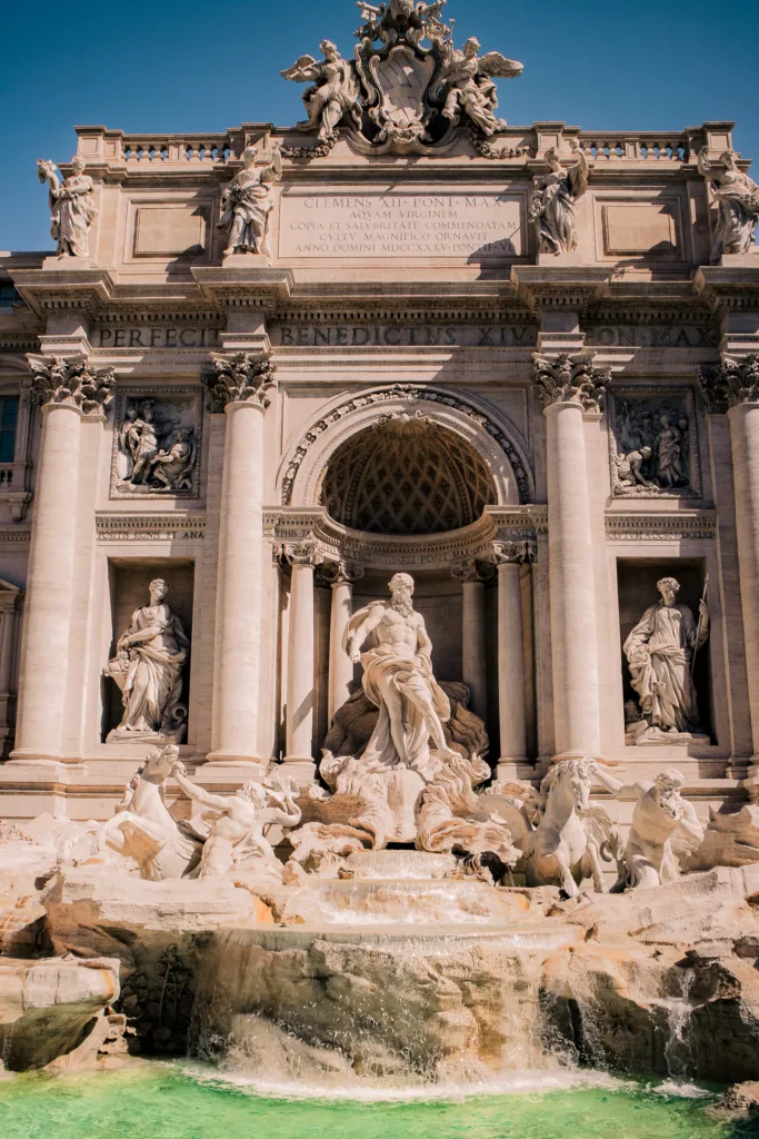 Fontanna di Trevi w Rzymie z monumentalnymi rzeźbami Neptuna, koni morskich i trytonów w słońcu, z turkusową wodą u podnóża