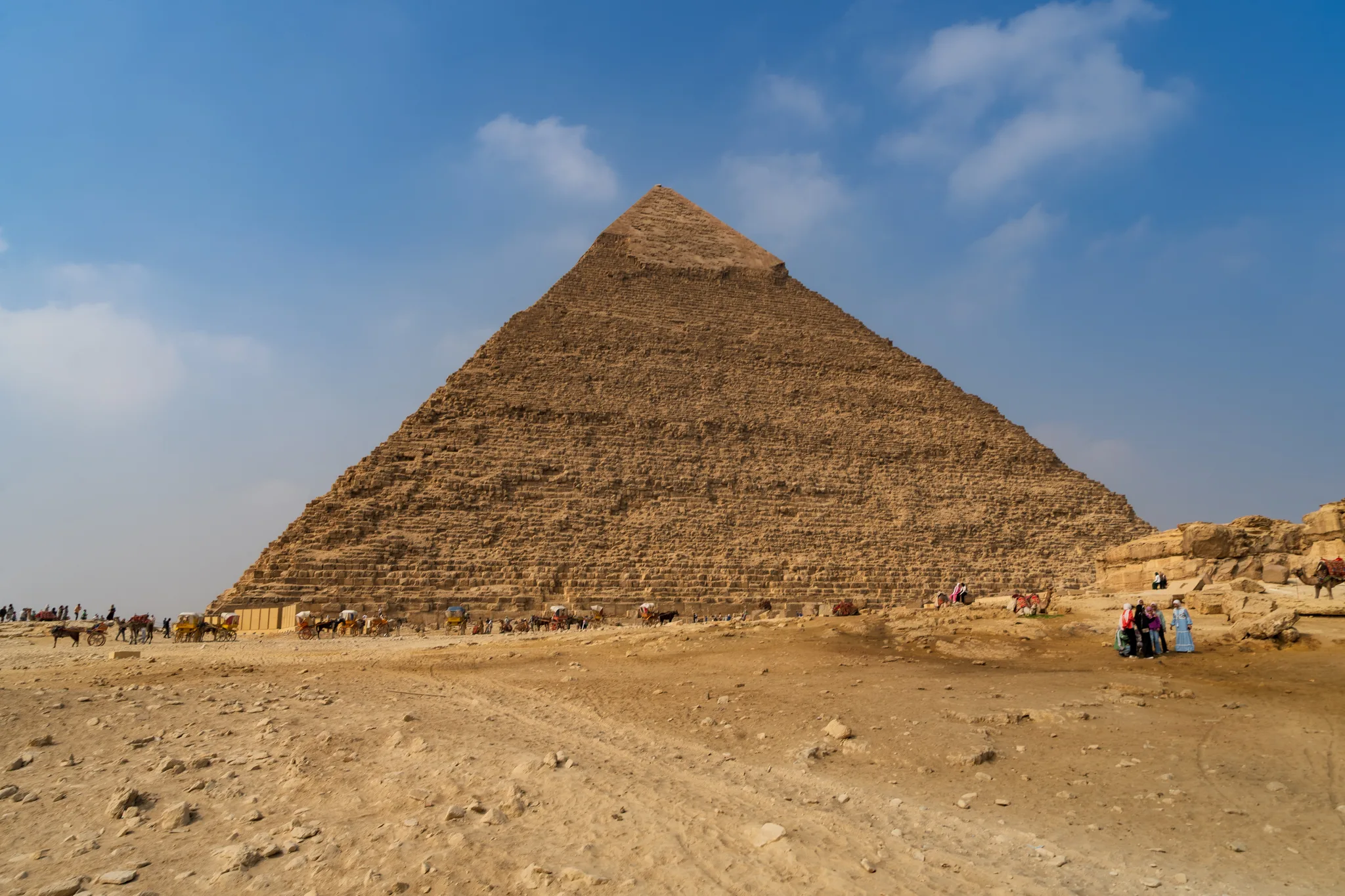 Piramida Chefrena na płaskowyżu Gizy widziana od frontu; u podnóża widać turystów oraz wielbłądy na pustynnym terenie - Wycieczka z Hurghady do Gizy.