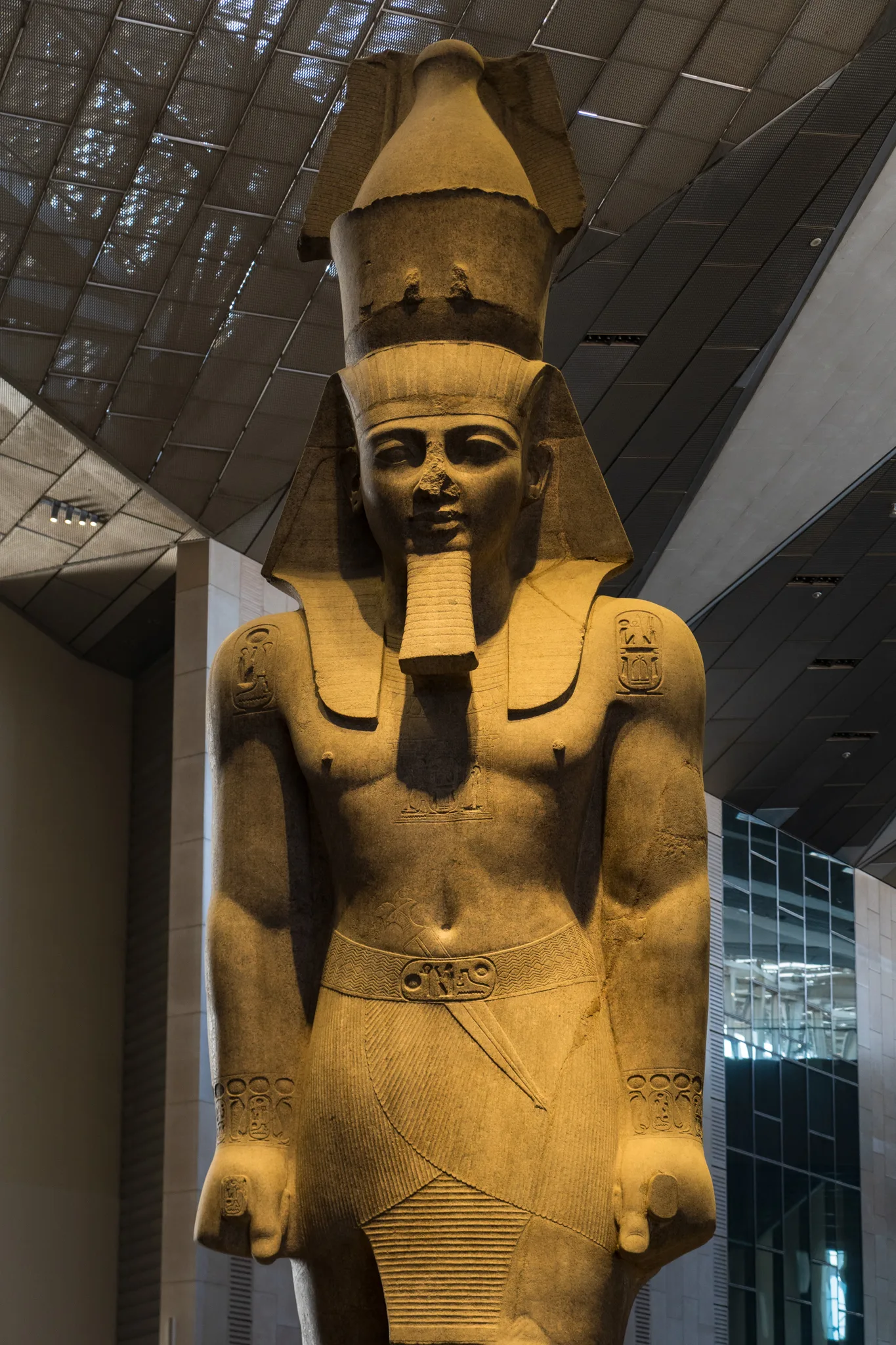 Monumentalny posąg faraona z królewską koroną, prezentowany w nowoczesnej sali egipskiego muzeum.