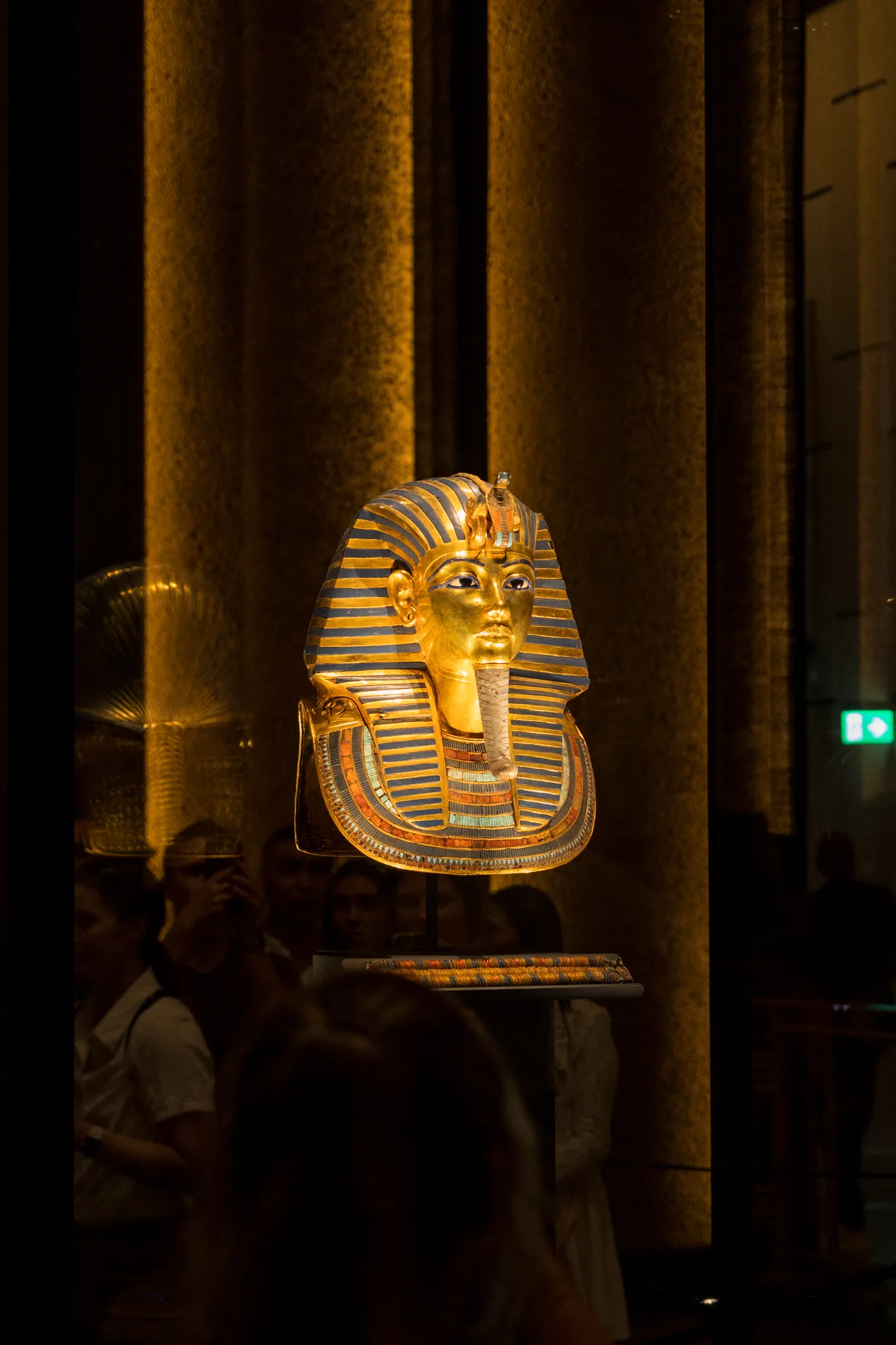 Złota maska pośmiertna Tutanchamona eksponowana w szklanej gablocie muzealnej, podświetlona ciepłym światłem.