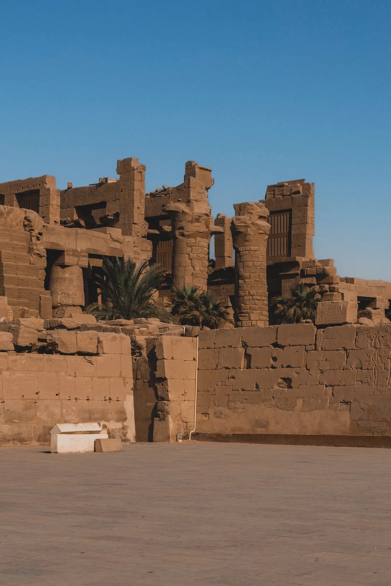 Monumentalny posąg faraona w świątyni Karnak, przedstawiony z krzyżowanymi ramionami i częściowo uszkodzoną twarzą.