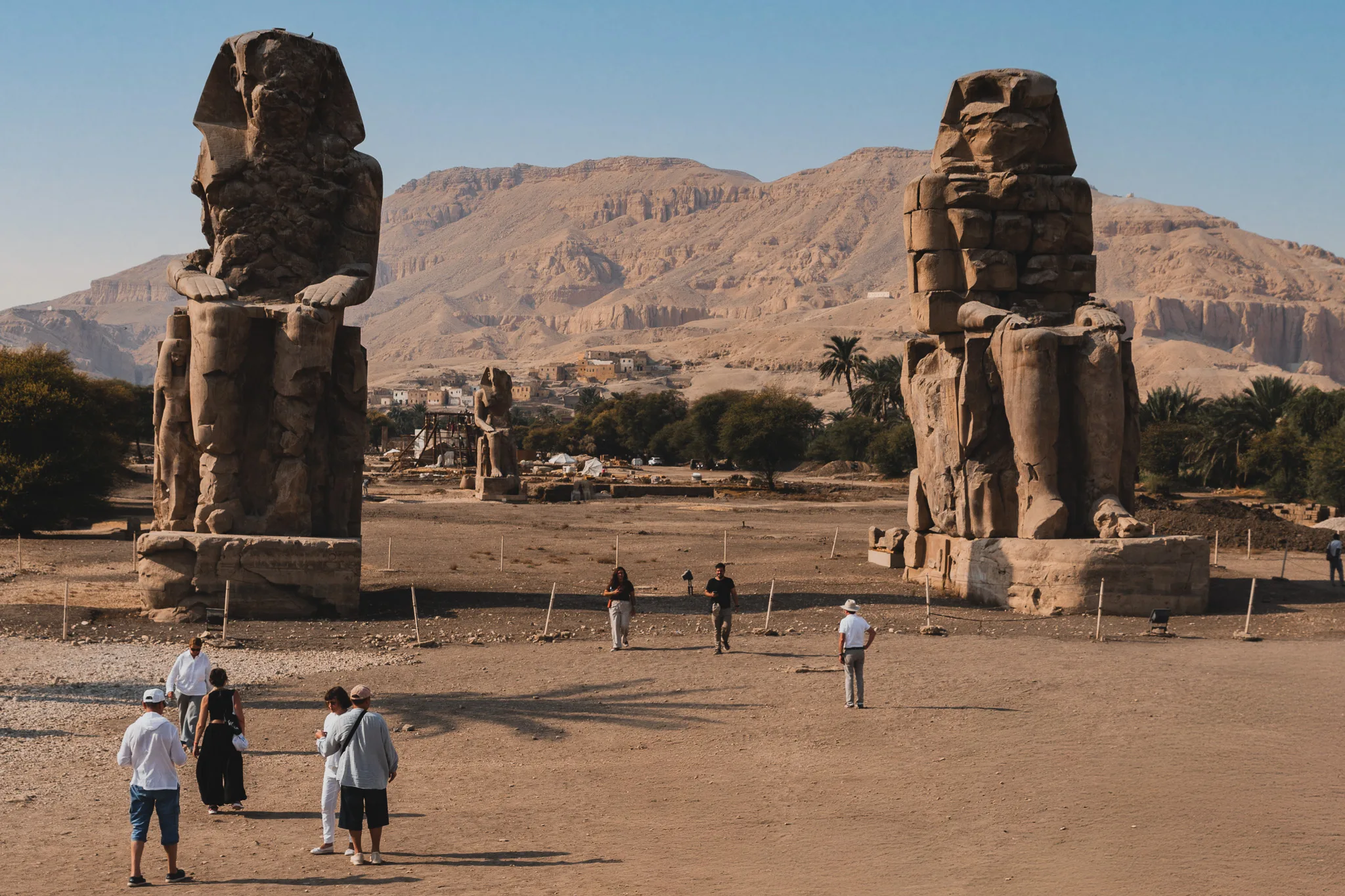 Kolosy Memnona w Luksorze na tle gór Teb Zachodnich, widok z placu z turystami.