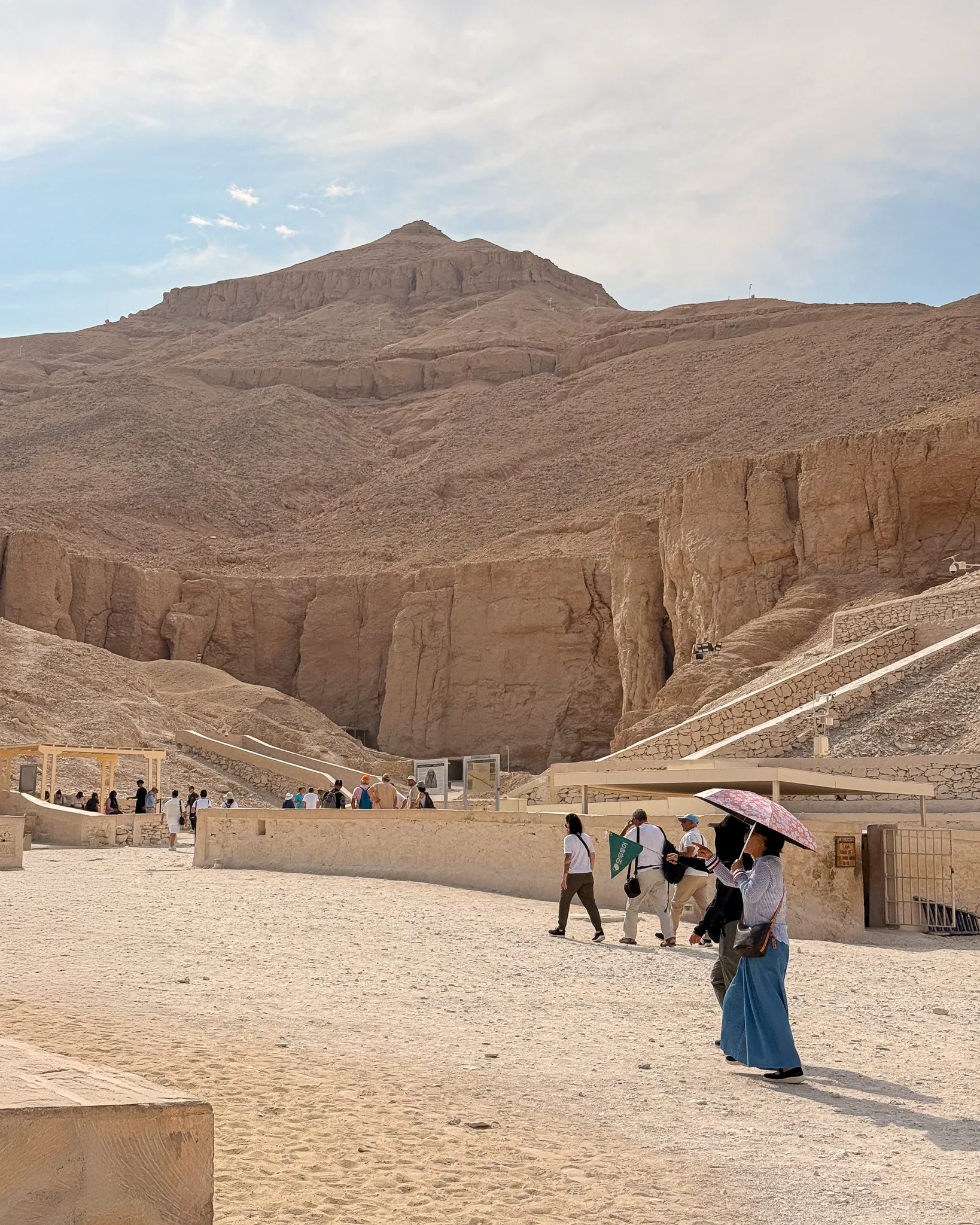 Wejście do Doliny Królów w Luksorze; turyści idą w stronę pawilonu wejściowego otoczonego skalistymi klifami.